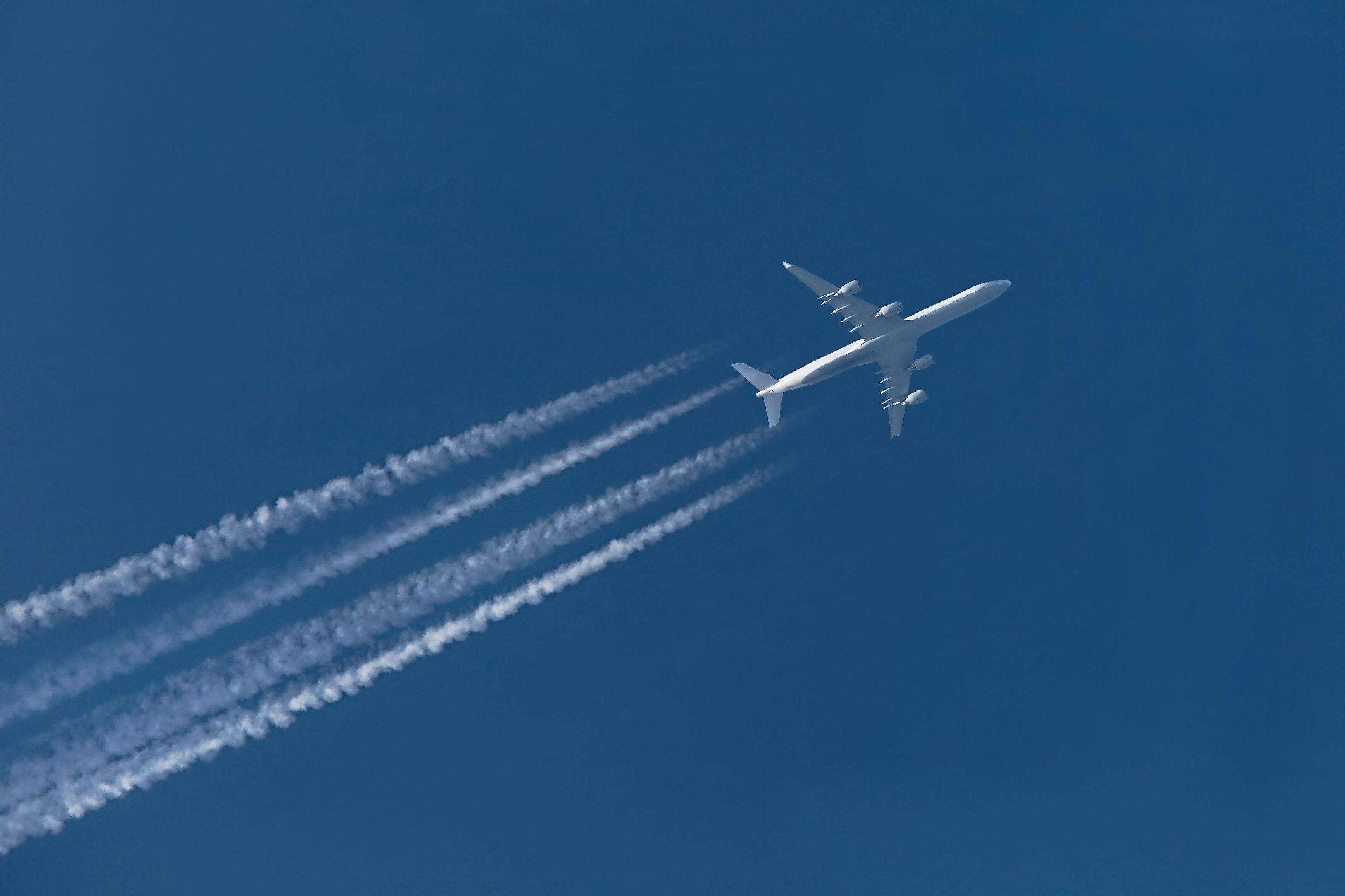 An aircraft flying seen from the ground leaving contrails as it moves through the sky.