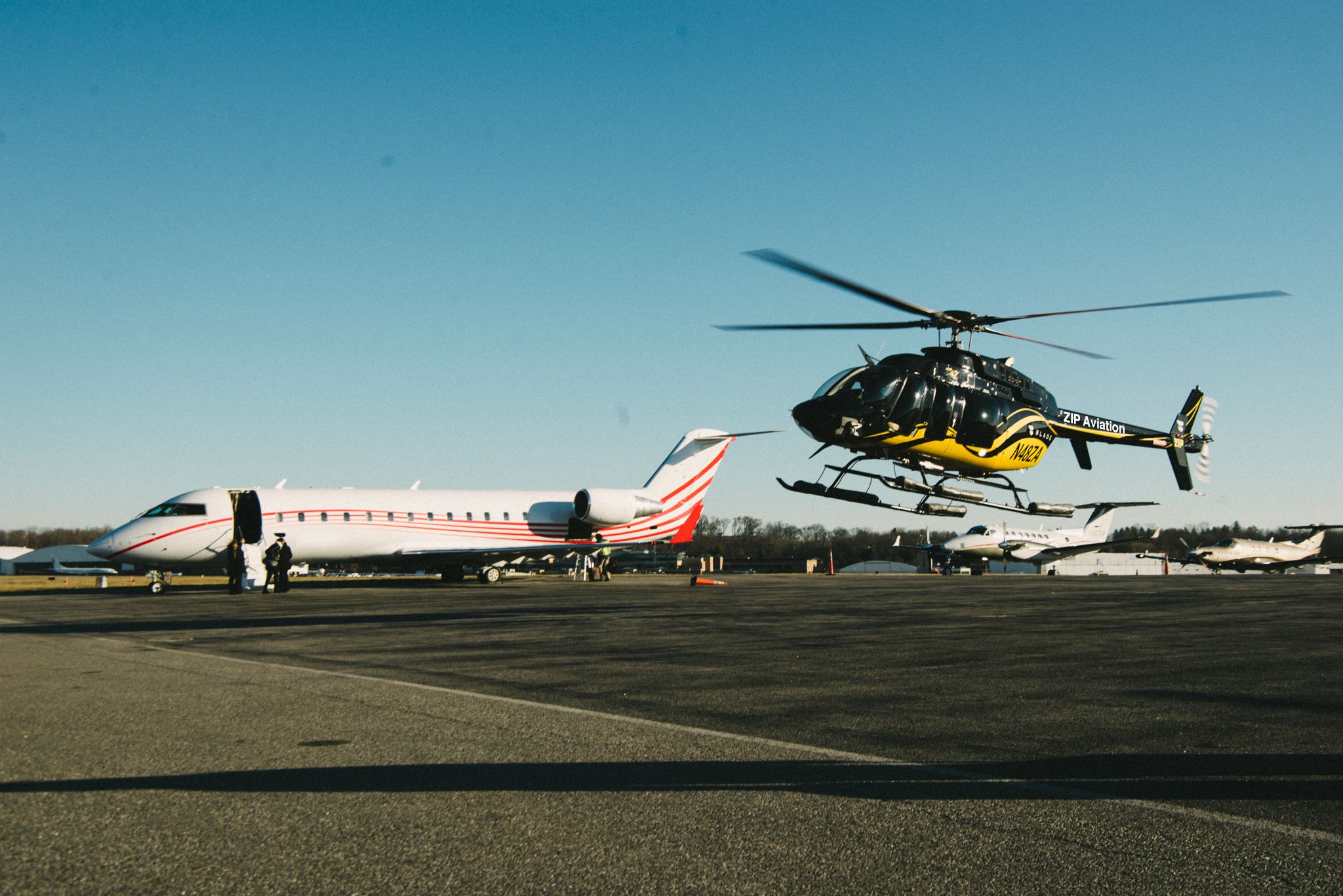 A helicopter taking off next to a business jet an an airfield.