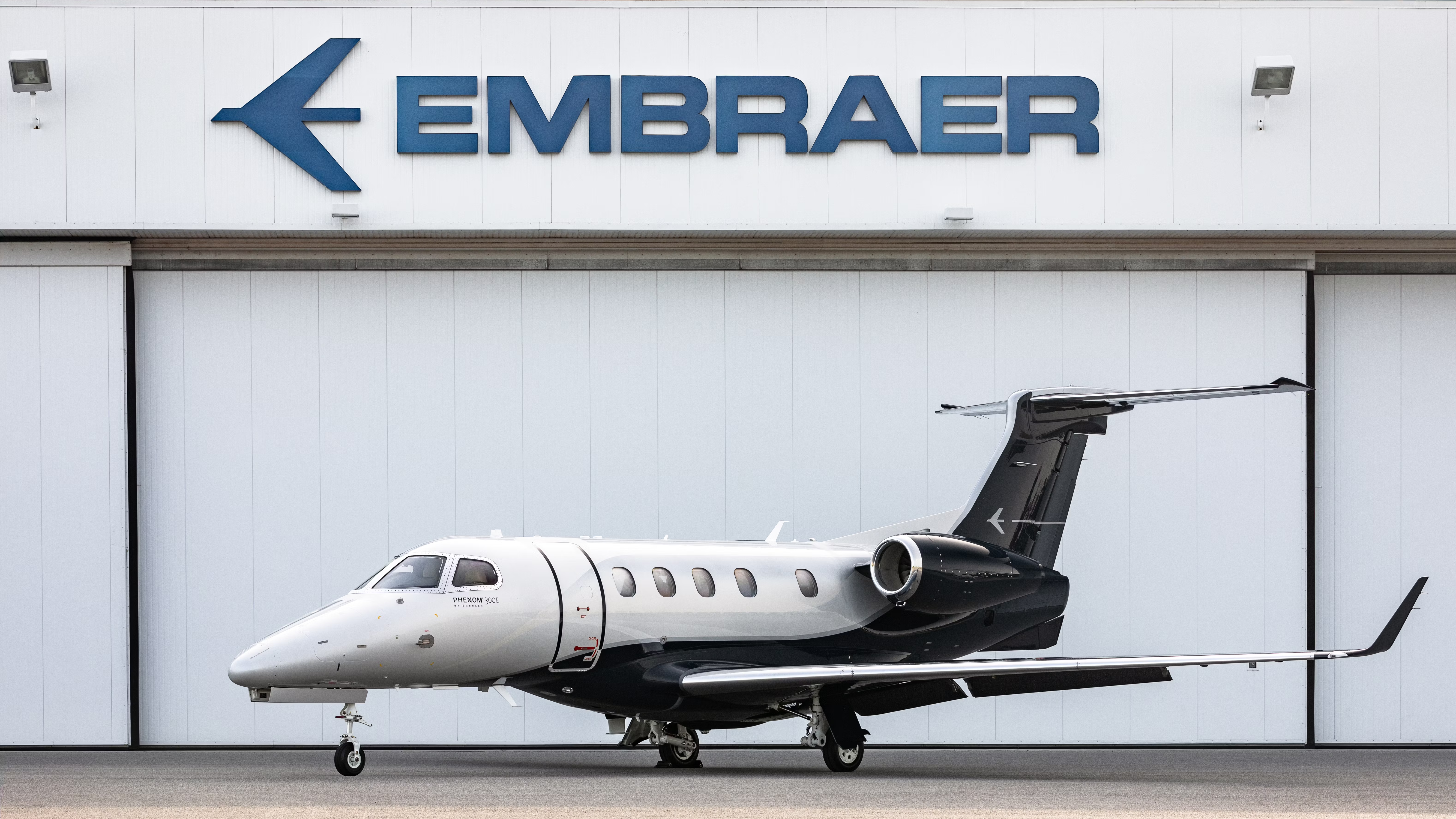 An Embraer Phenom 300E parked right outside of an aircraft hangar.