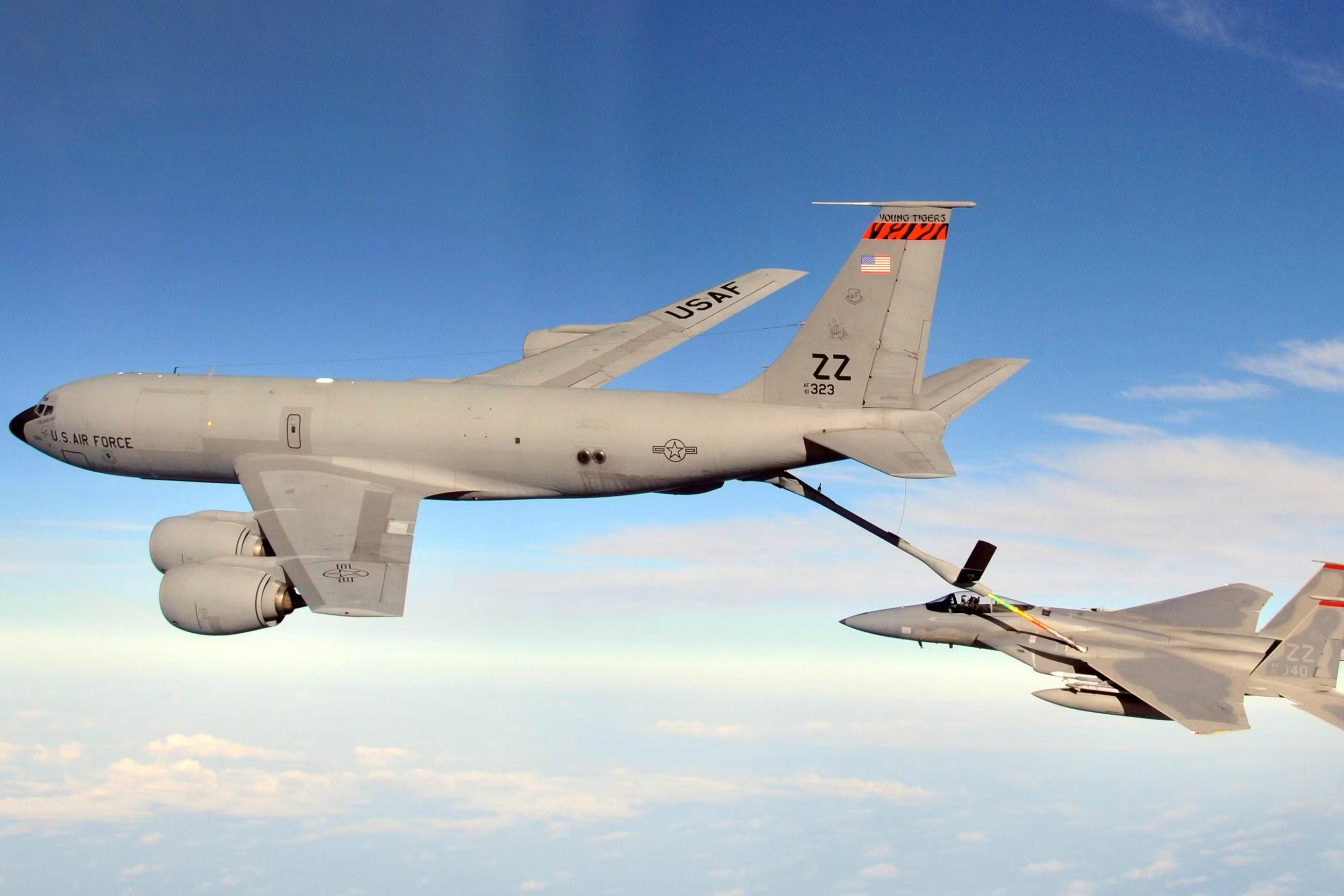 A KC-135 flying with its refueling boom attached to a fighter jet.