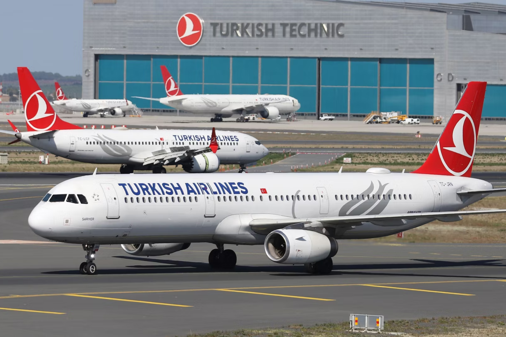 Four Turkish Airlines Aircraft taxiing or parked at an airport, with a Turkish Technic hangar in the background.
