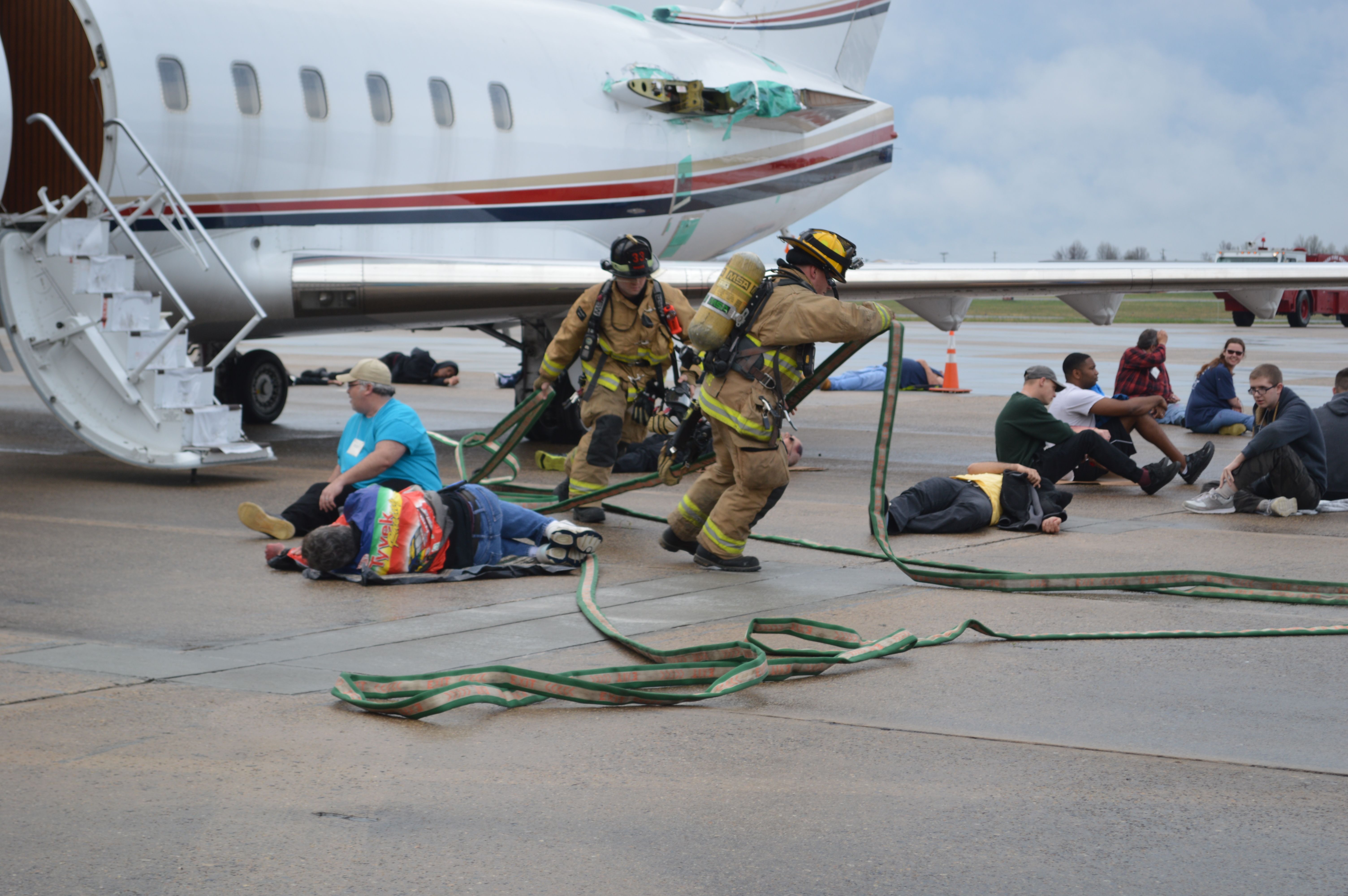 Airport firefighters run a training drill, with several fake injured passengers near a parked business jet.