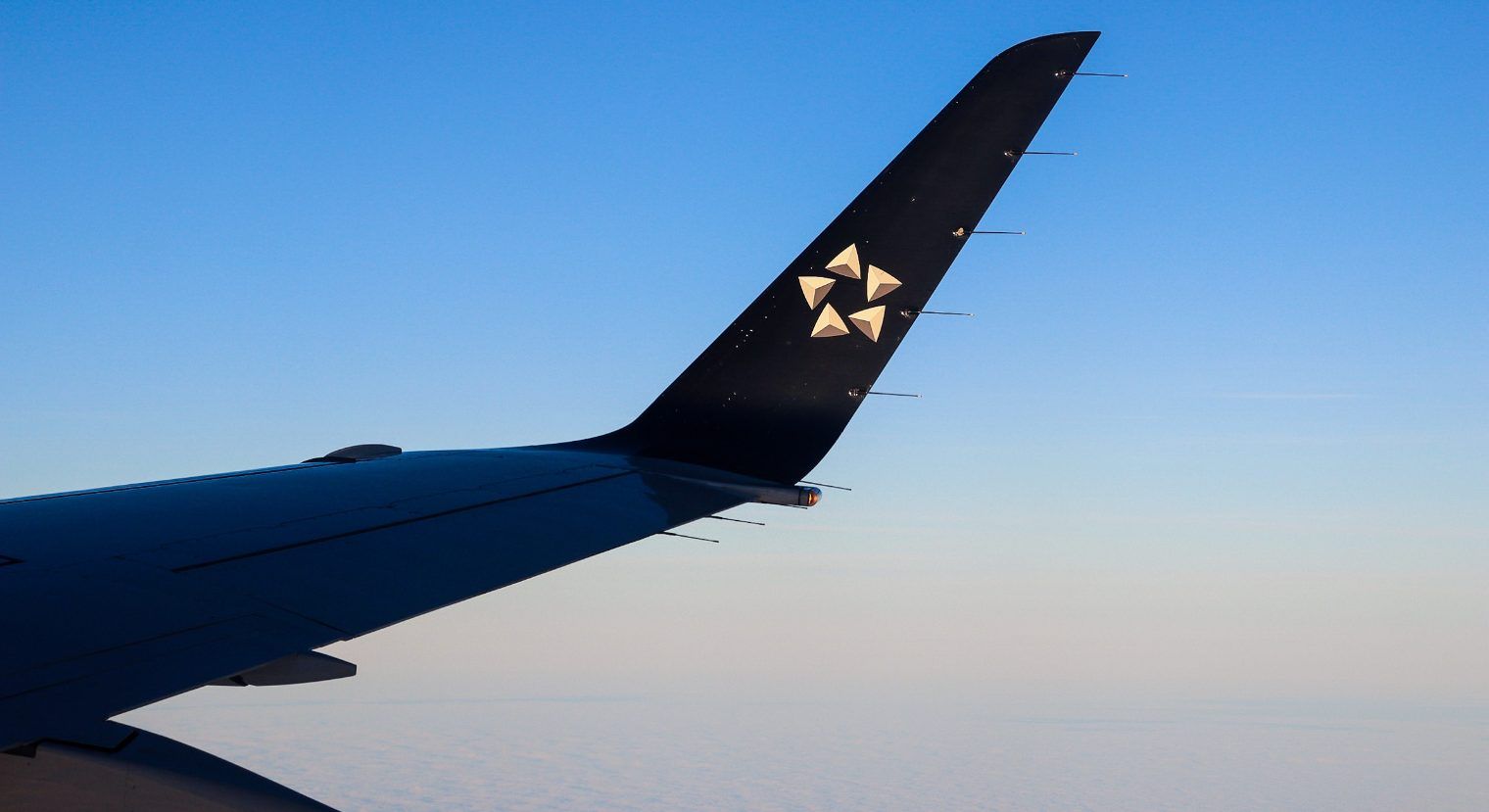 A Star Alliance Logo on the wing of a LOT Polish Airlines Embraer E170 flying in the sky.