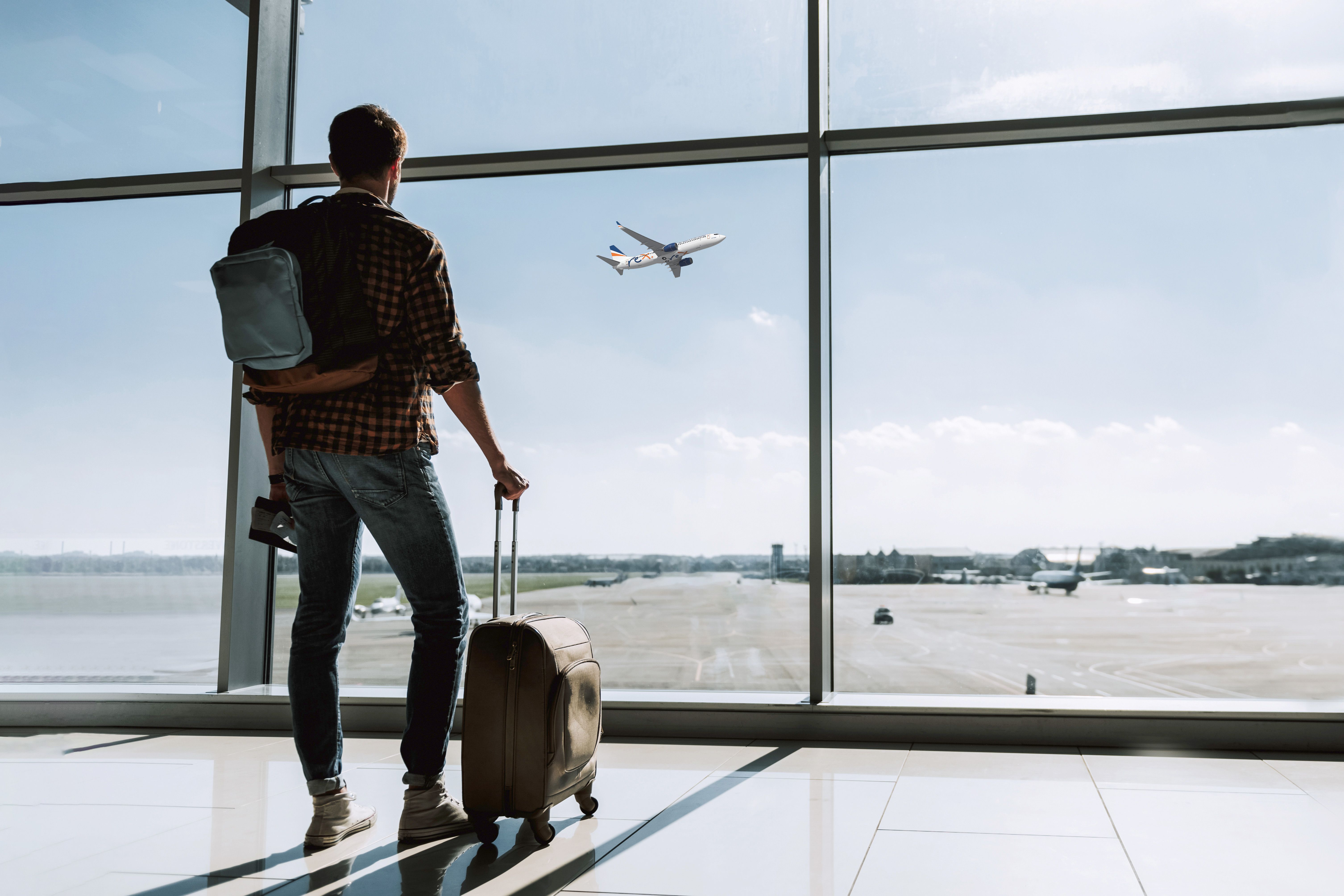 A Passenger looking out an airport terminal window, watching an aircraft take off.