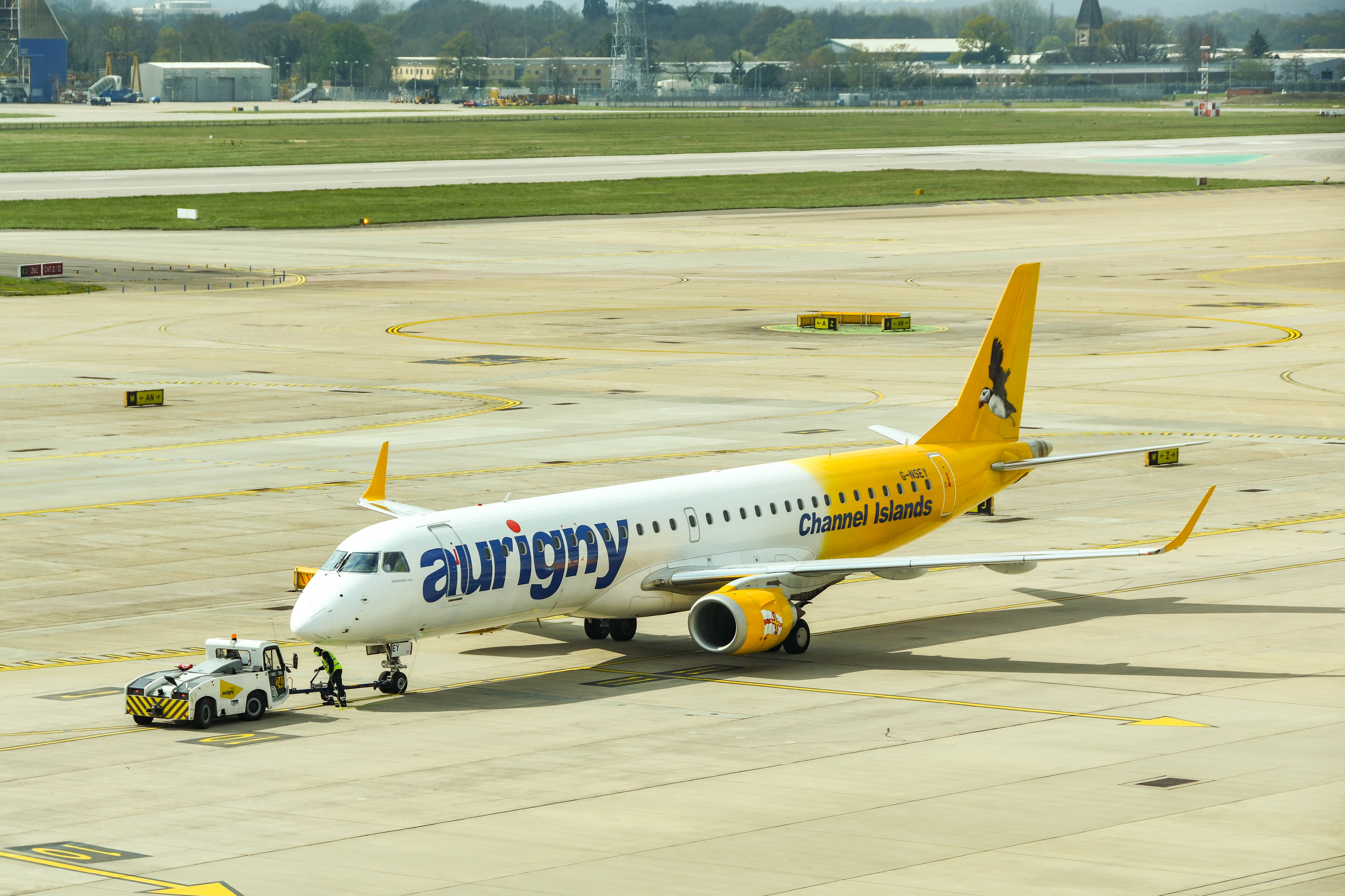 An Aurigny Embraer E195 being pushed by a ground vehicle at London Gatwick Airport.