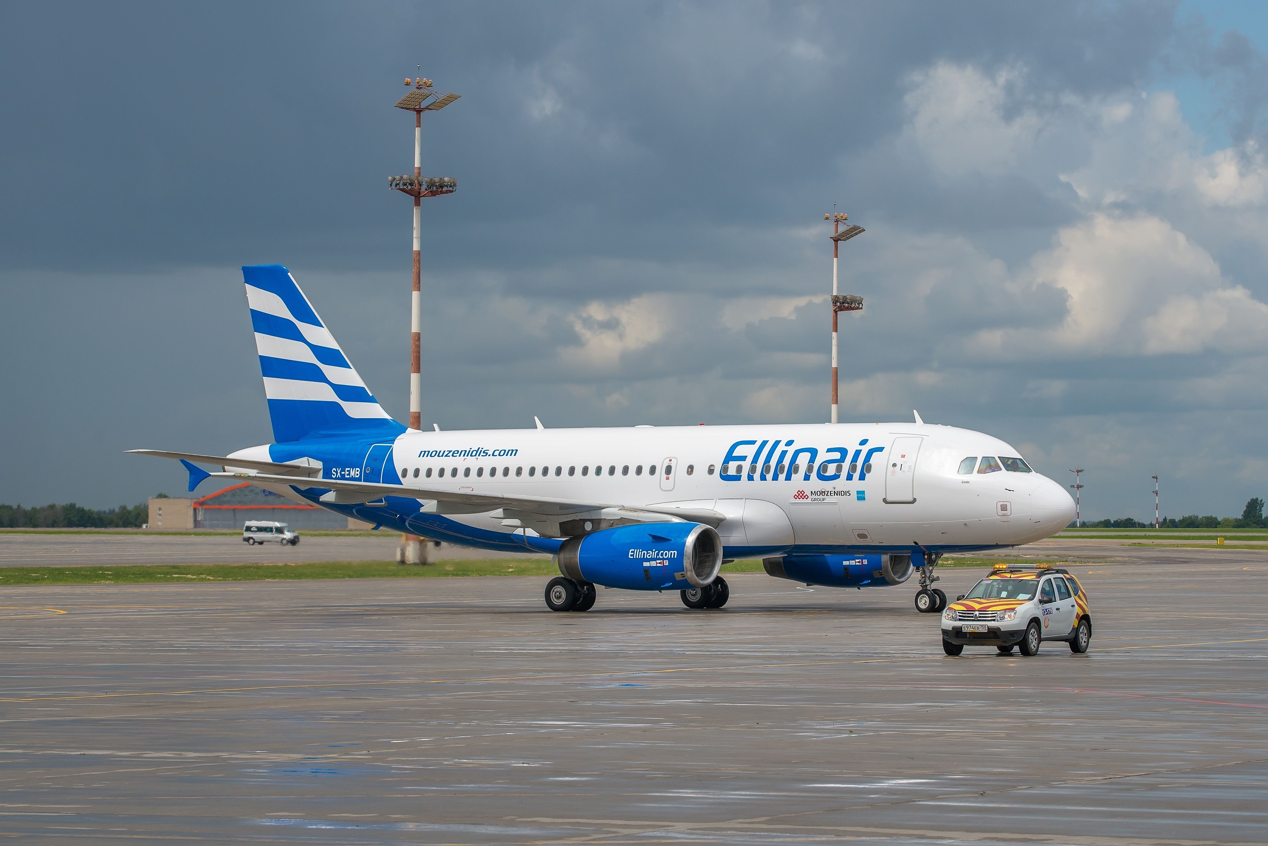 An Ellinair Airbus A319 and Follow Me Car on an airport apron.