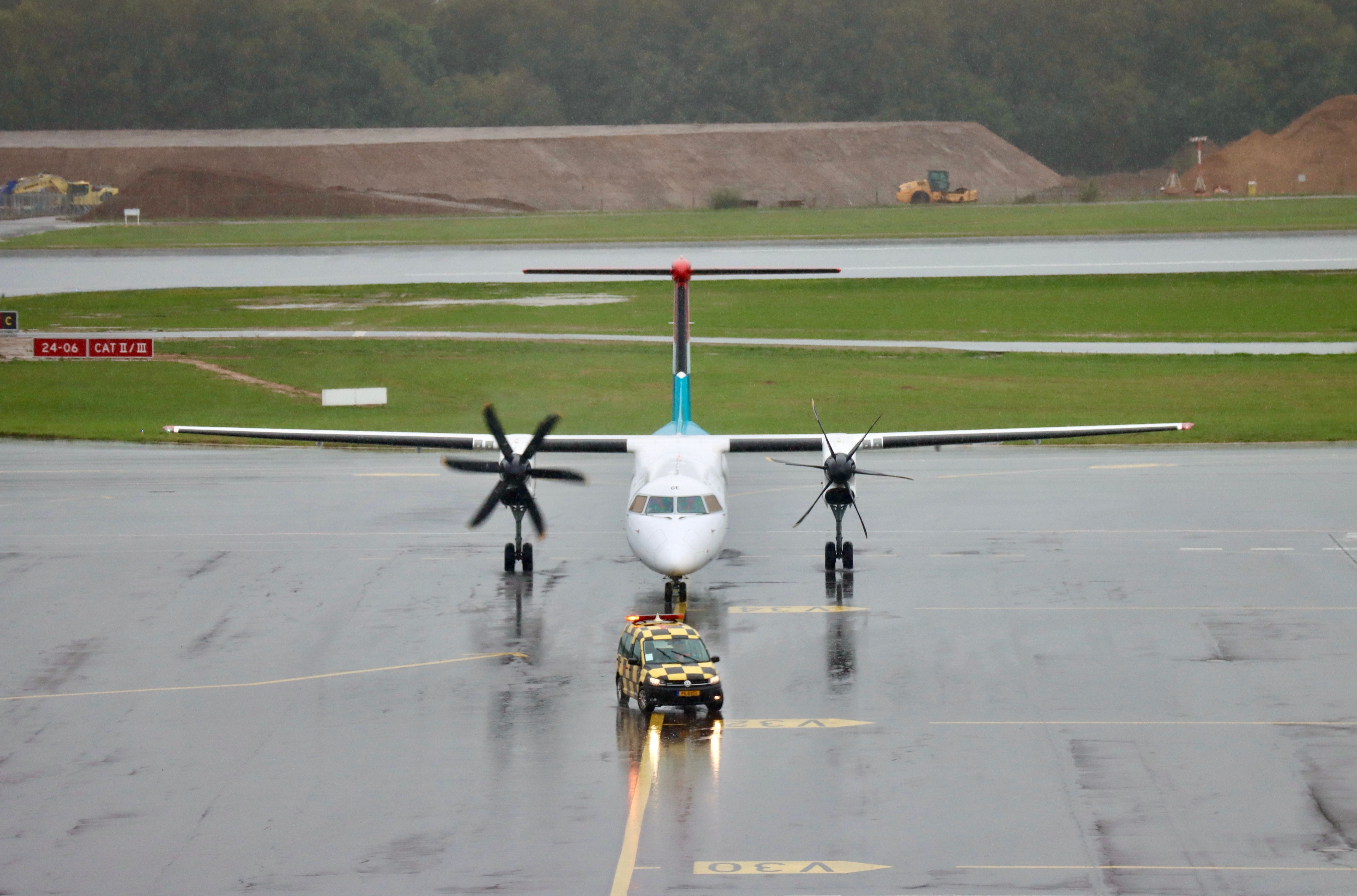 A Luxair Dash 8 Turboprop behind a Follow-Me Car on an airport apron.