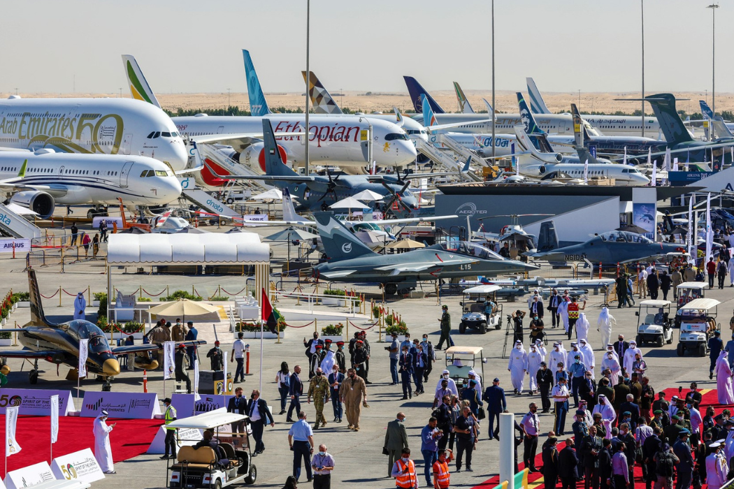 Several military and commercial aircraft surrounded by people at the Dubai Air Show.