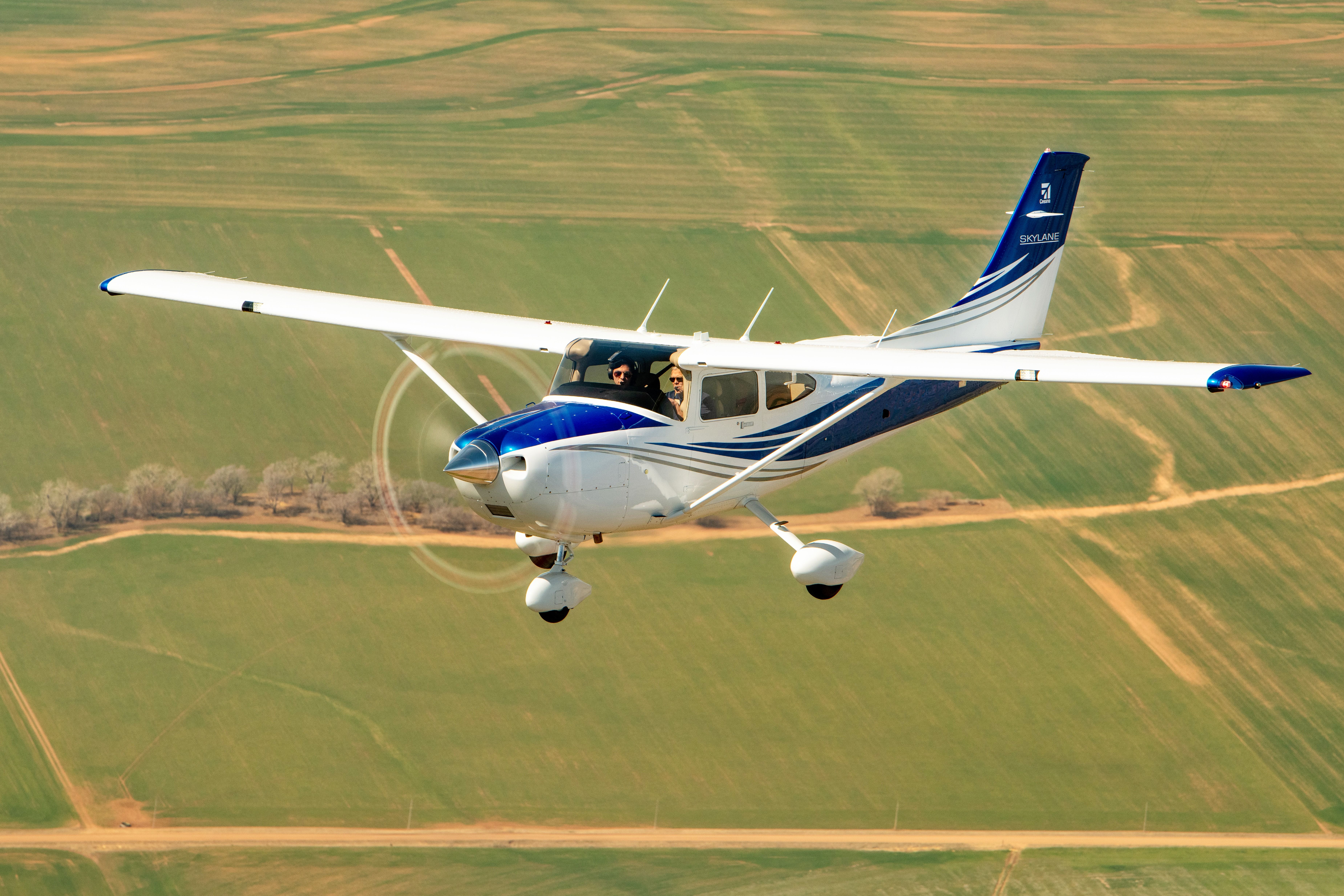 A Cessna 182 Skylane flying above a farm.