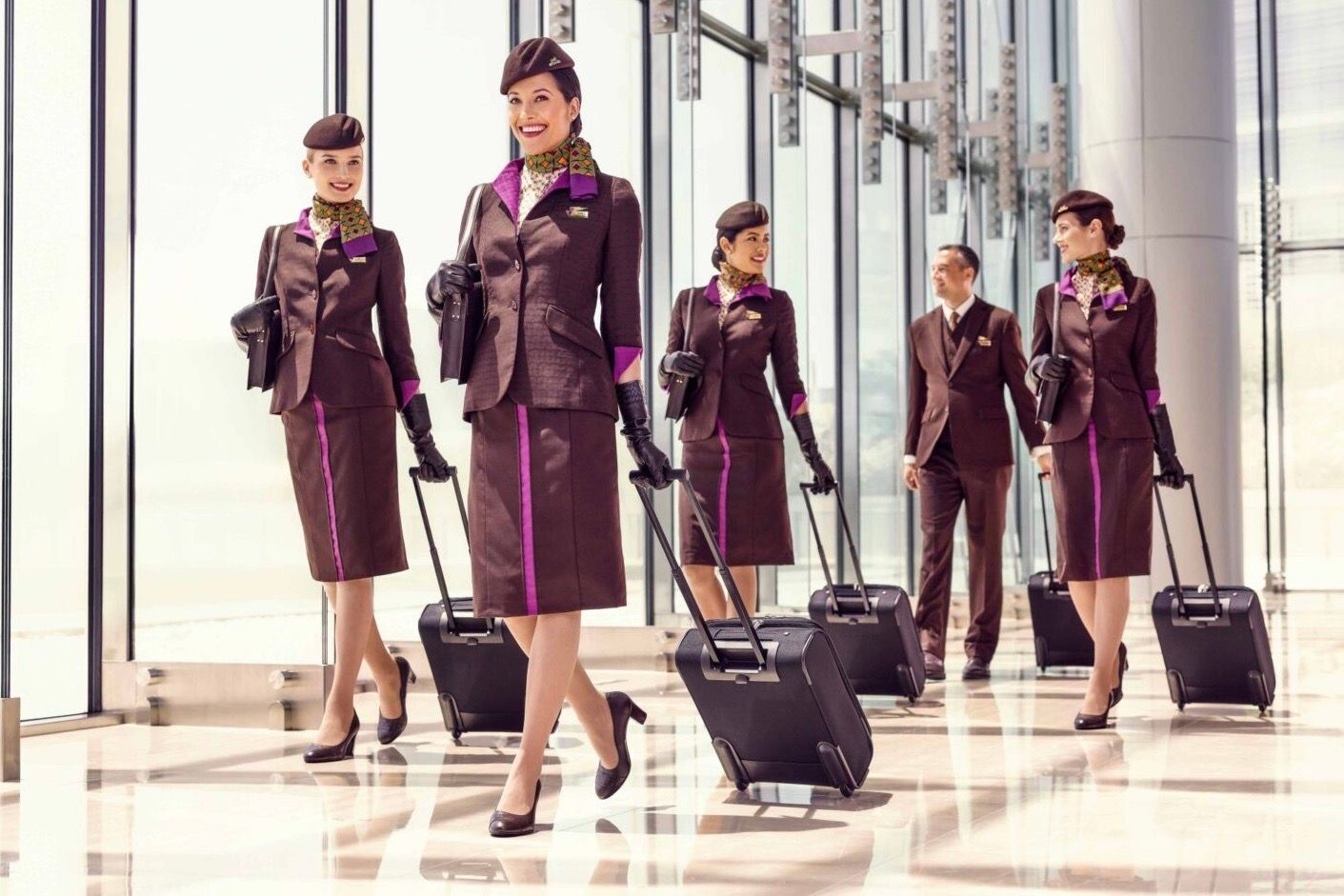Several Etihad Airways cabin crew members walking through an airport with suitcases.