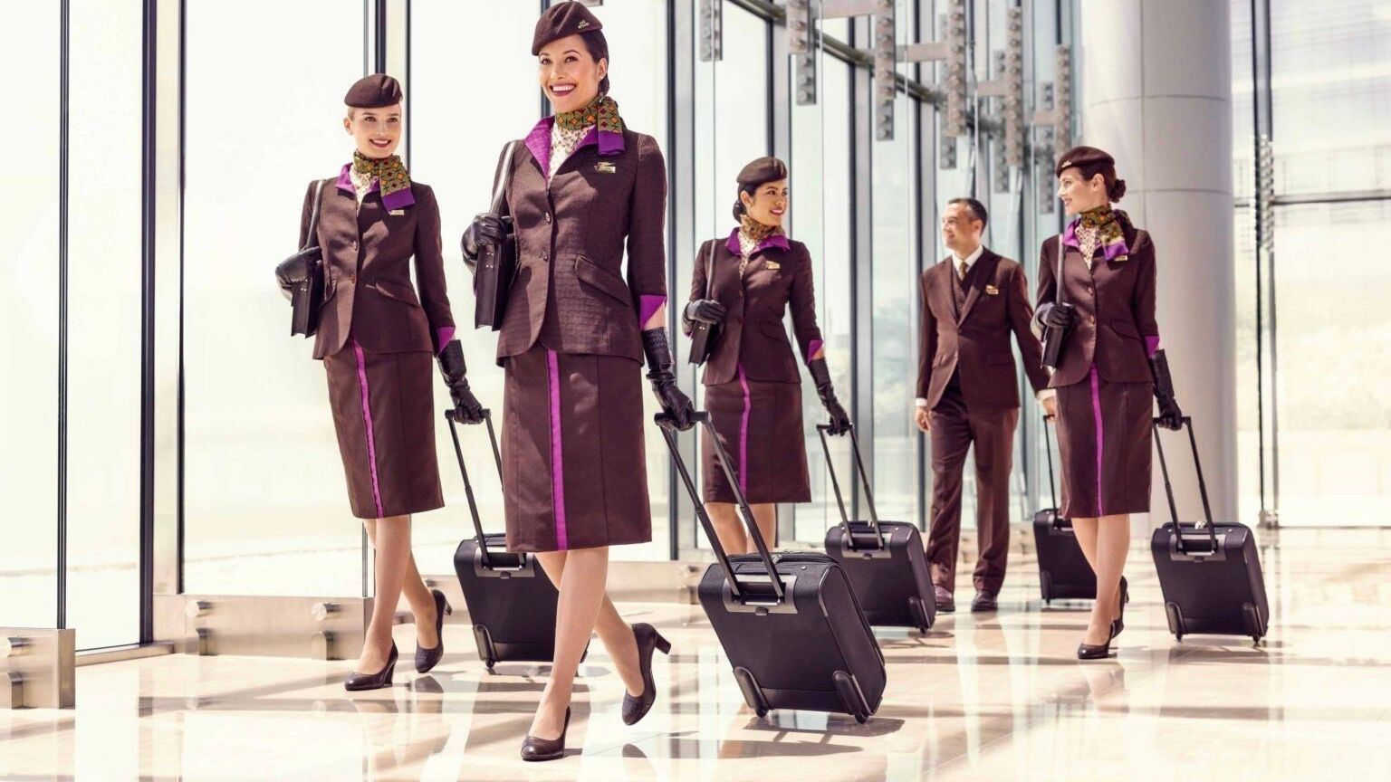 Several Etihad Airways cabin crew members walking through an airport with suitcases.