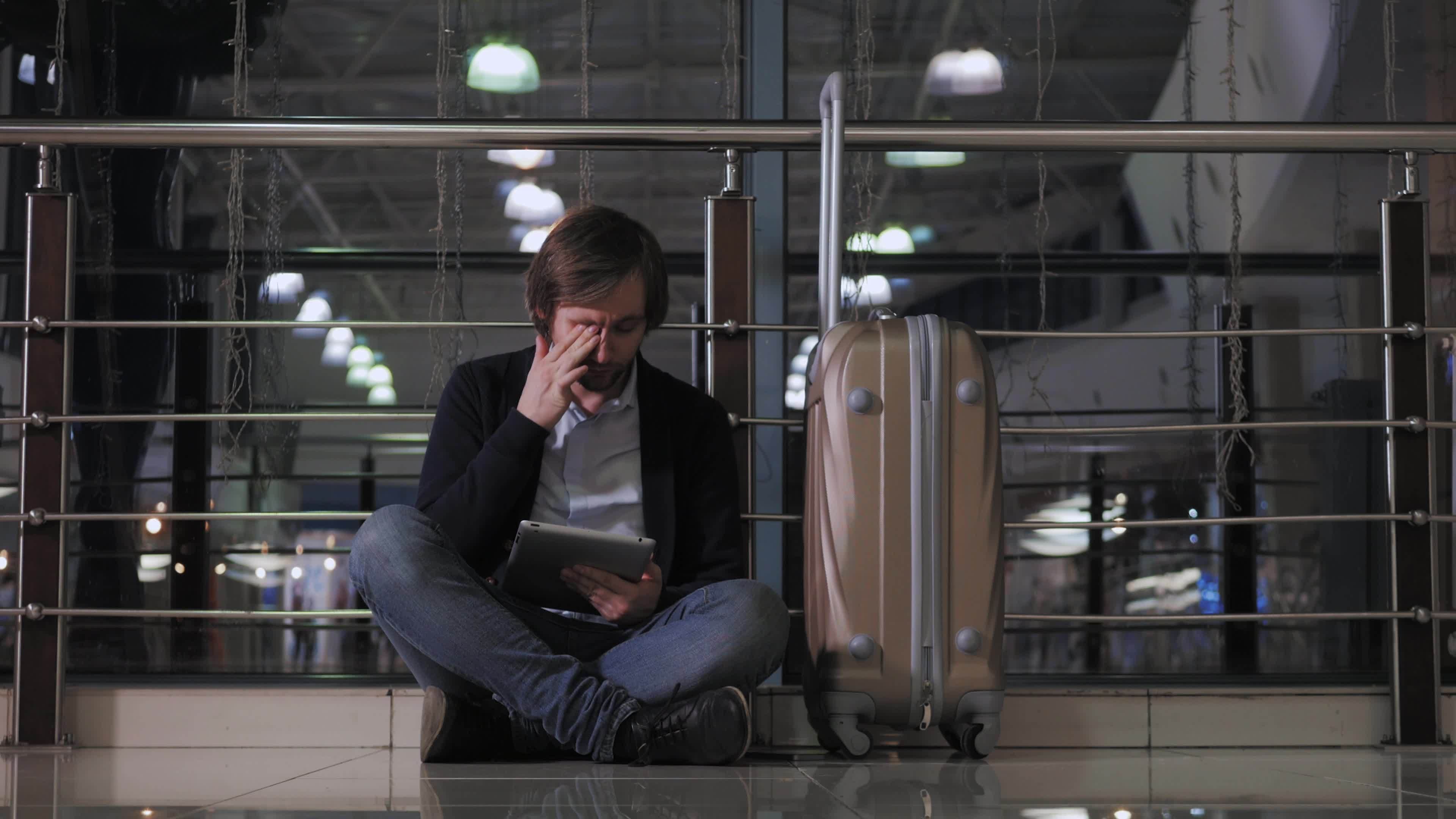 A passenger with his luggage sitting in an airport during the night 