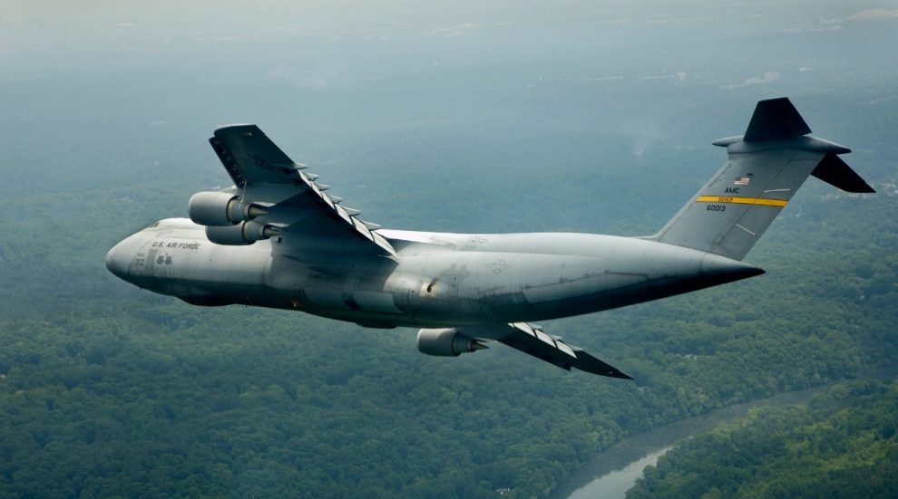 A Lockheed C-5 Galaxy making a turn in the air flying over a forest.
