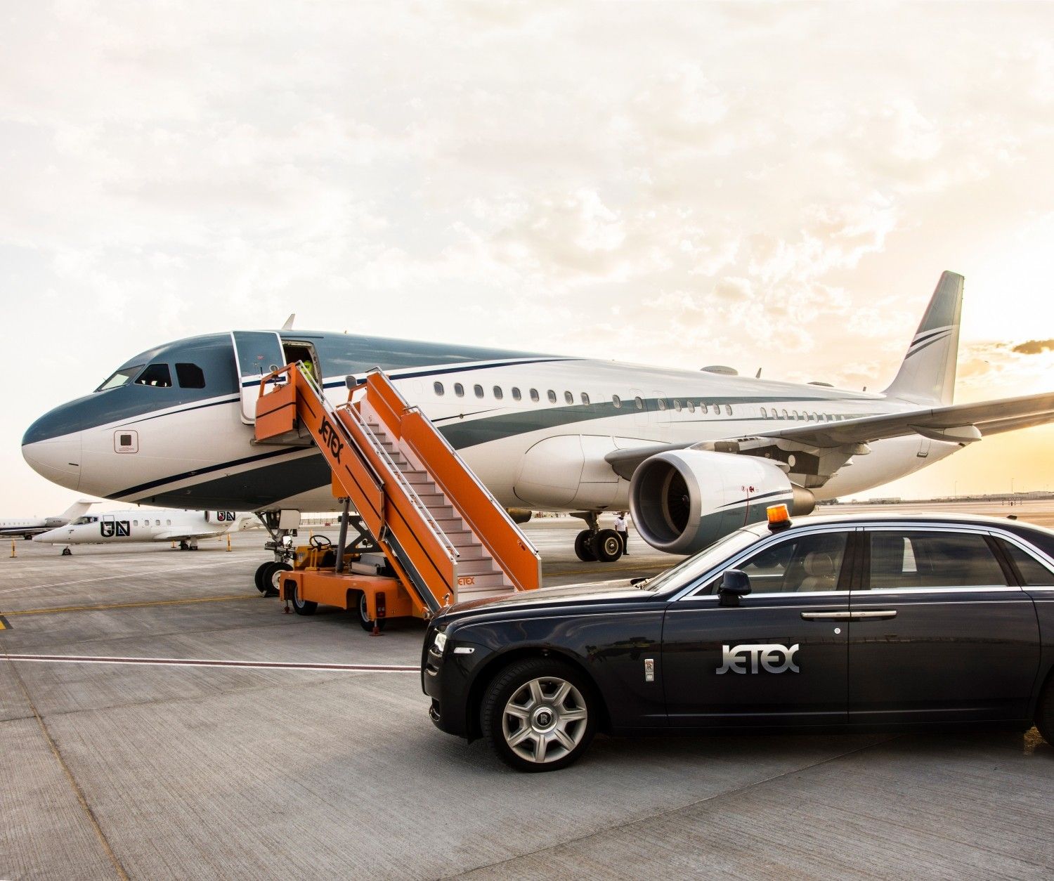 A Jetex car parked near a large business jet parked on an airport apron.