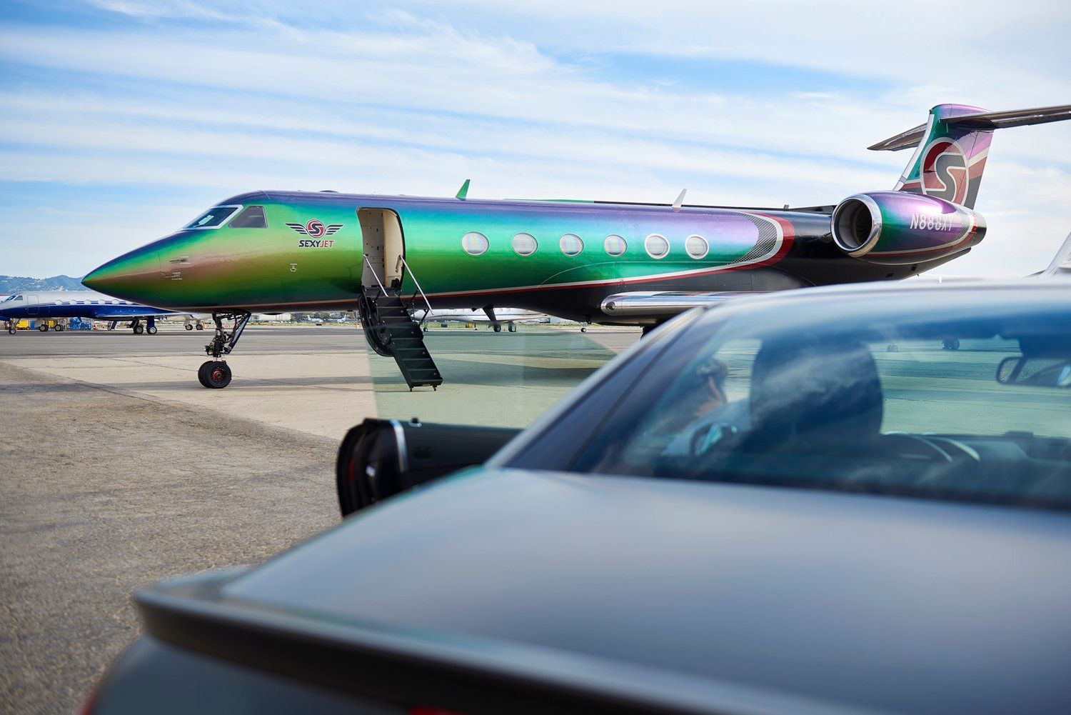 A closeup of a car parked near the SexyJet Gulfstream GV.