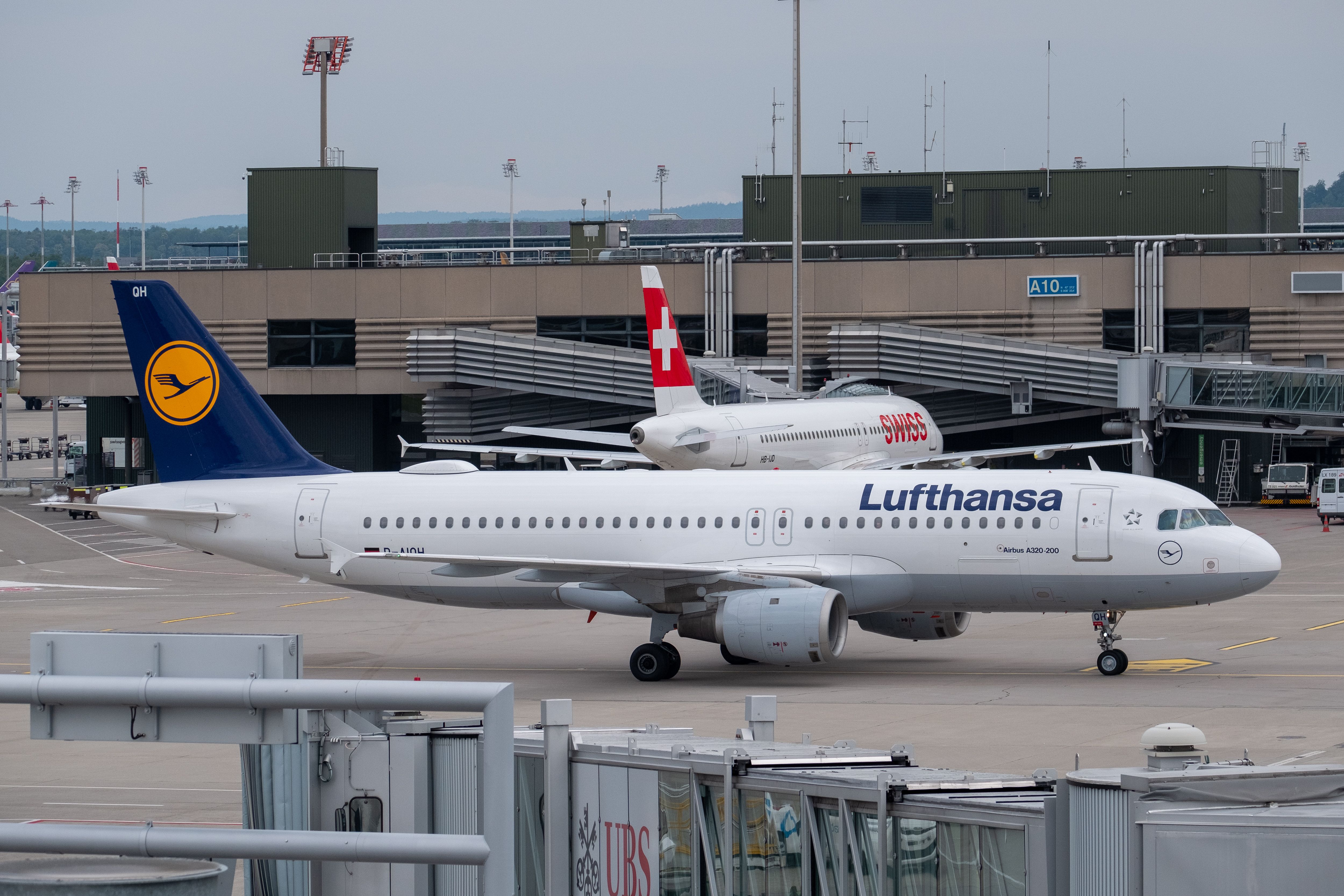 A Lufthansa aircraft taxiing in front of a SWISS aircraft parked at an airport gate.