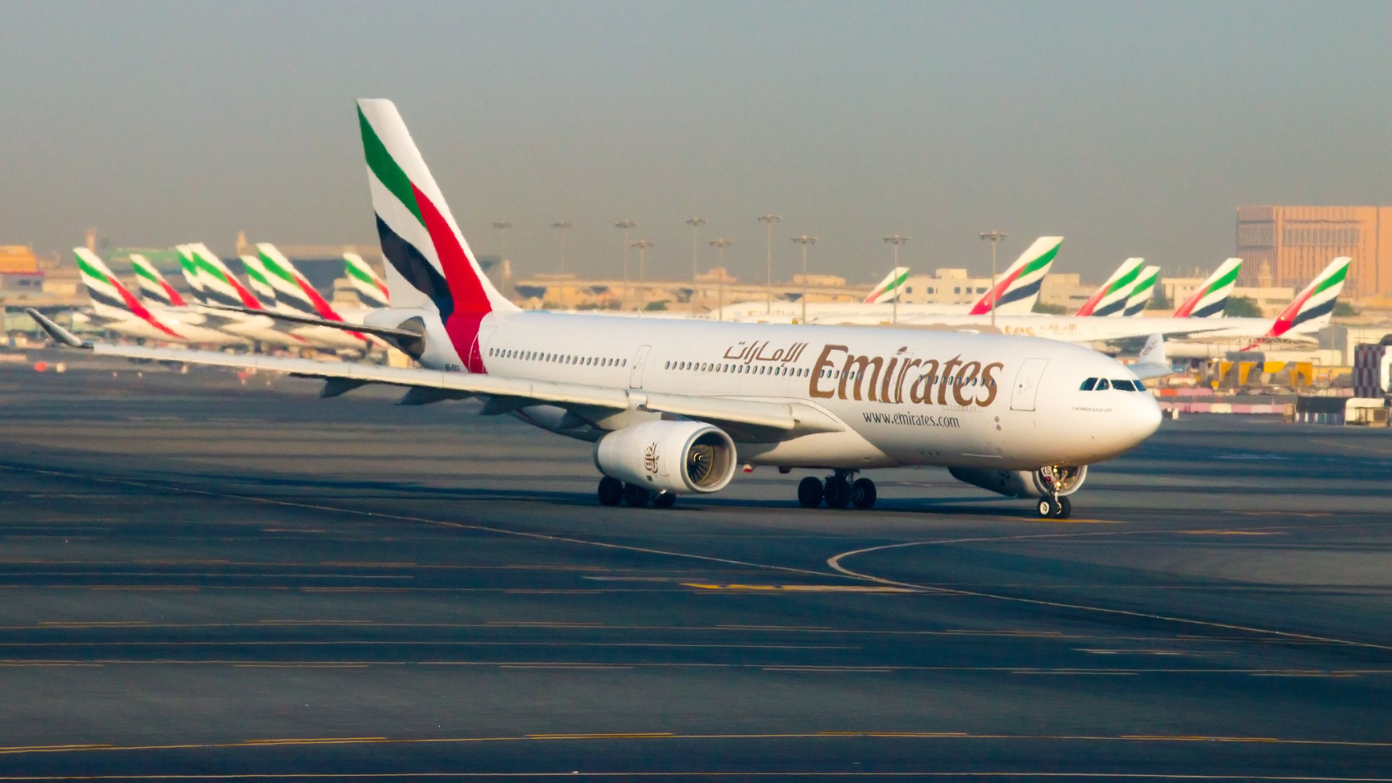 An Emirates Boeing 777 on the Dubai International Airport apron, in front of several parked Emirates aircraft.