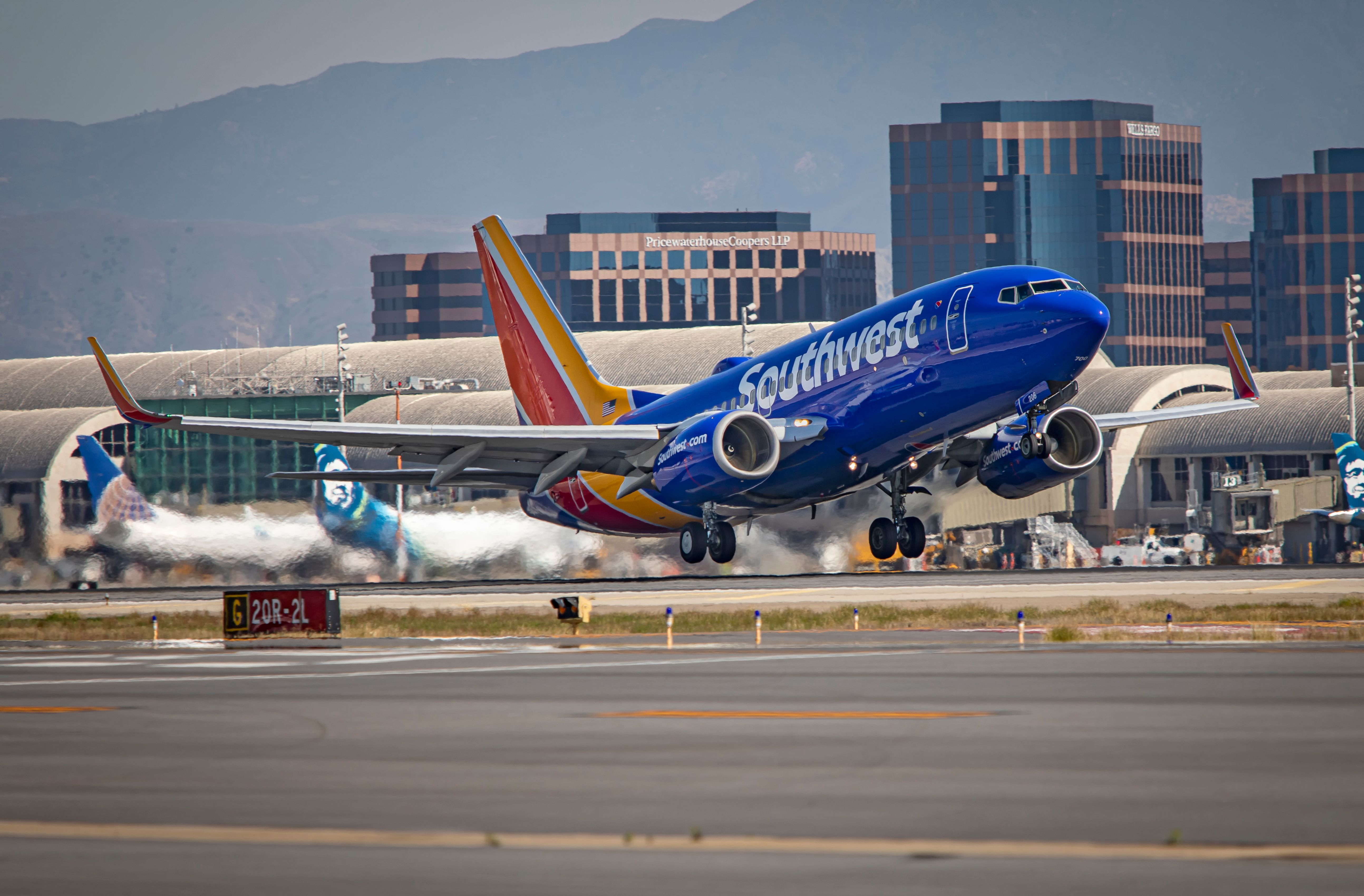 Shutterstock_1666141843 - SANTA ANA, CA/USA - 03/02/20: A Southwest Airlines airliner takes off at John Wayne Airport with planes and buildings in Irvine, California in the distance