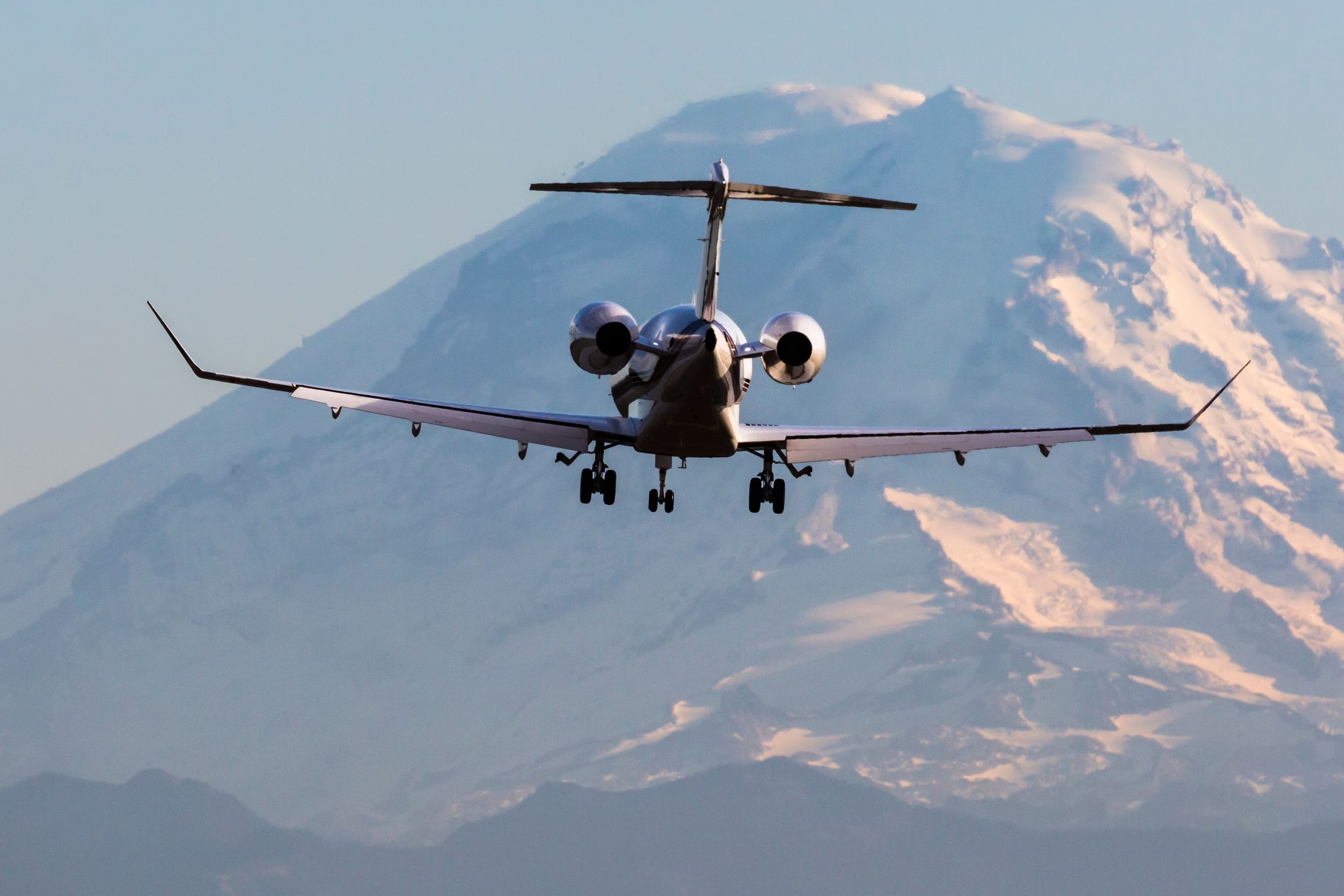 A Business jet flying in the sky, with a mountain in the background.