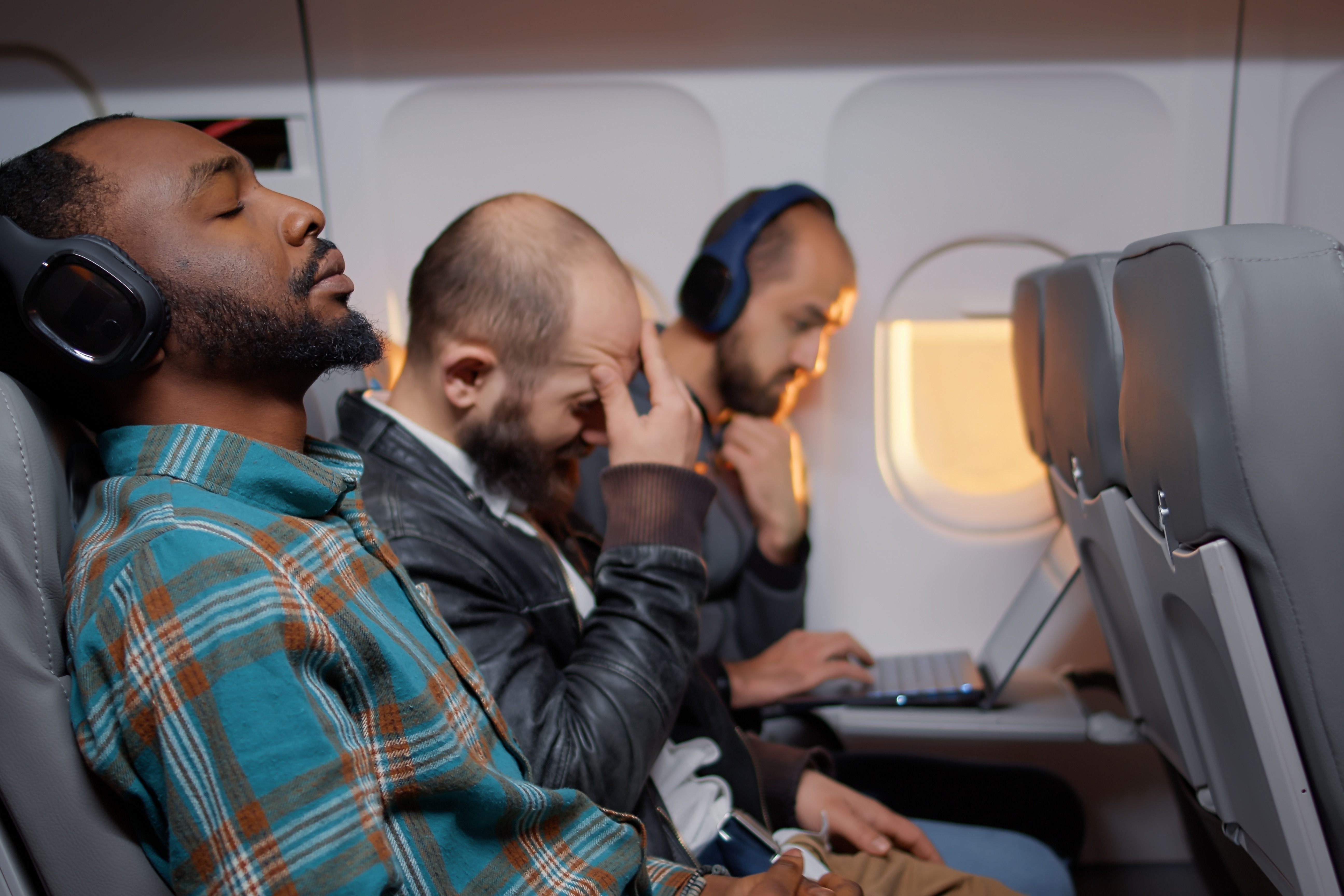 Three Passengers sitting in an economy class row on an aircraft.