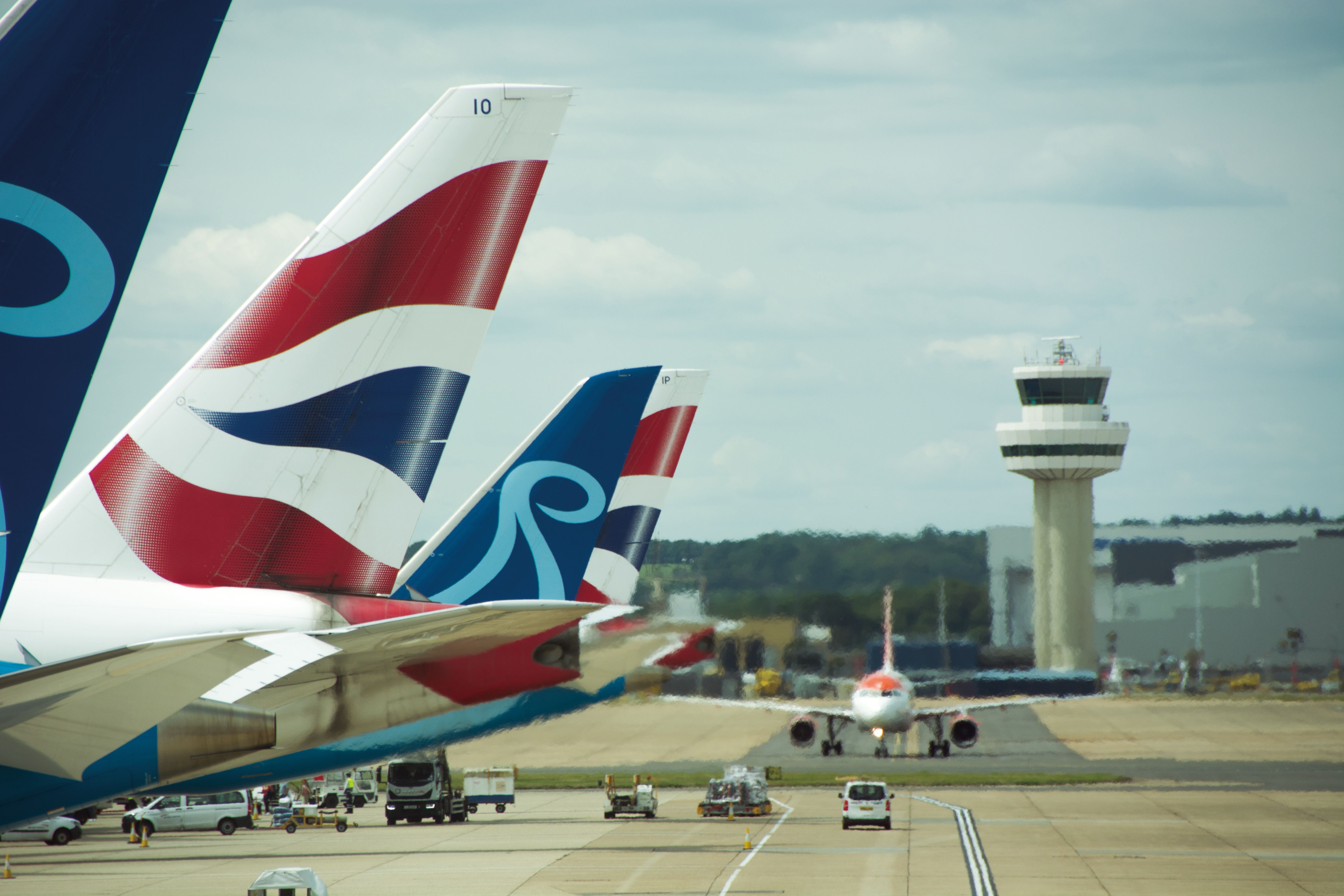 The tails of several British Airways and Norse Atlantic aircraft parked on an airport apron.
