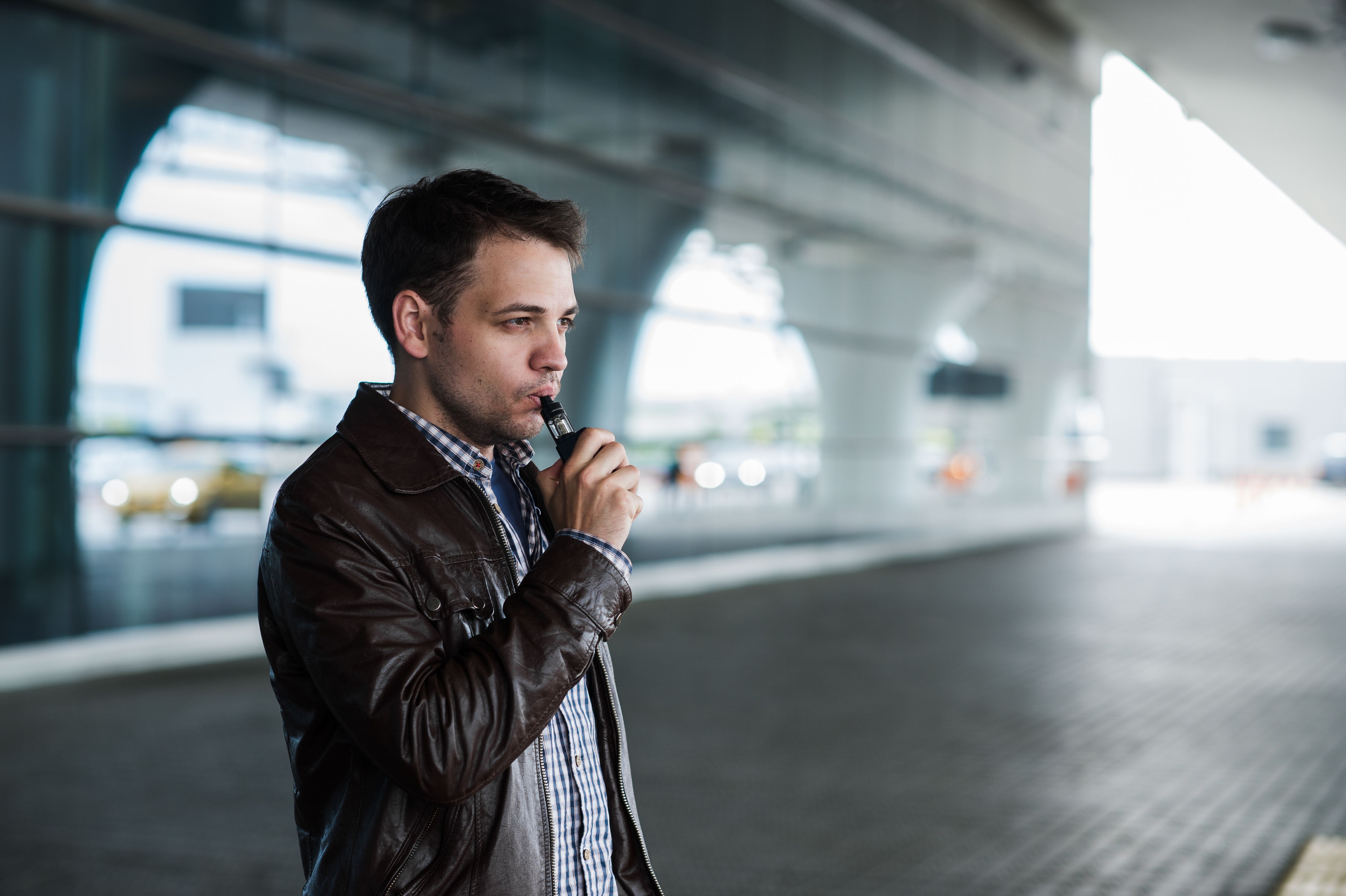 A Man using a vape outside of an airport terminal.