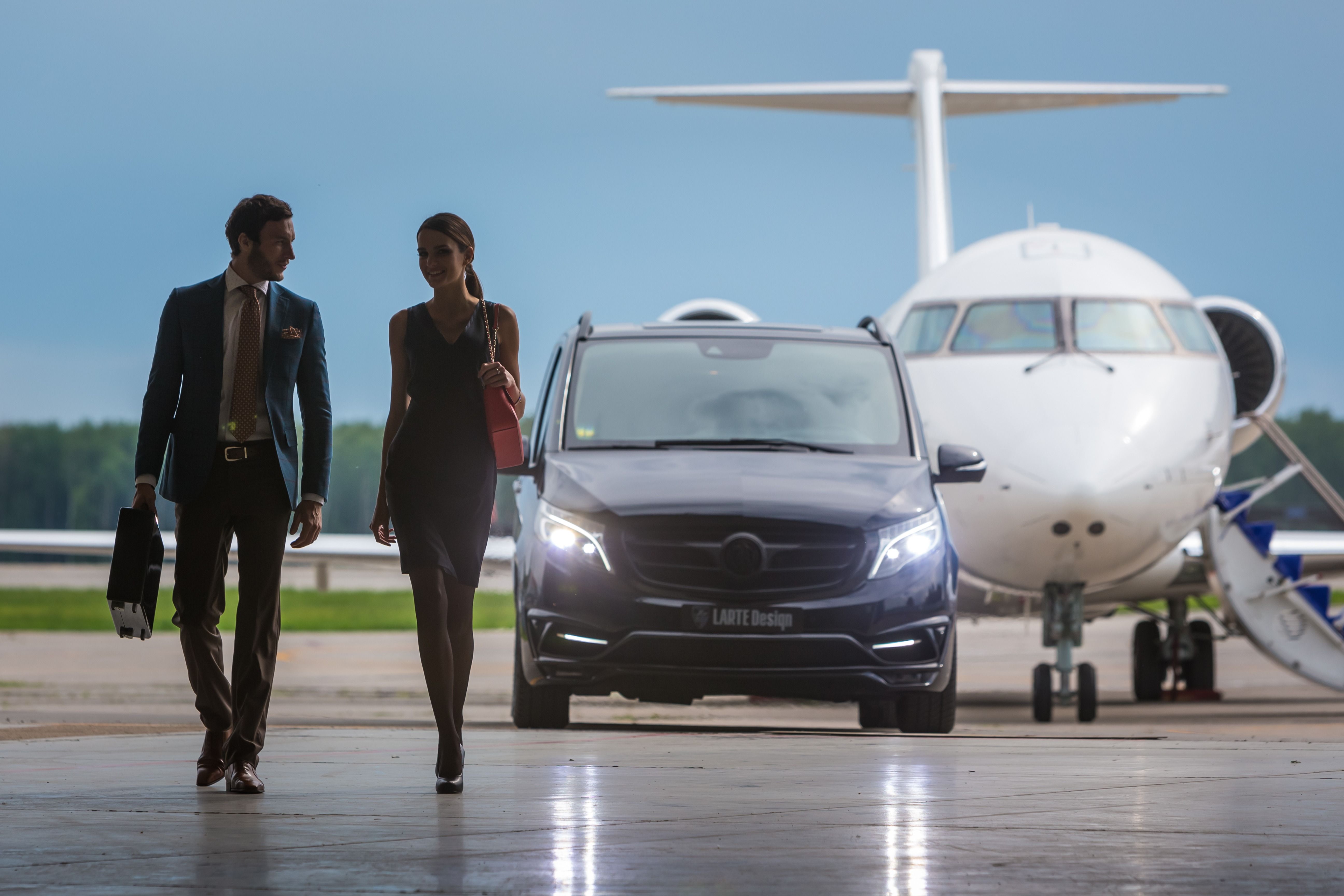 Two individuals in business attire walking away from a private aircraft parked on an airport apron.