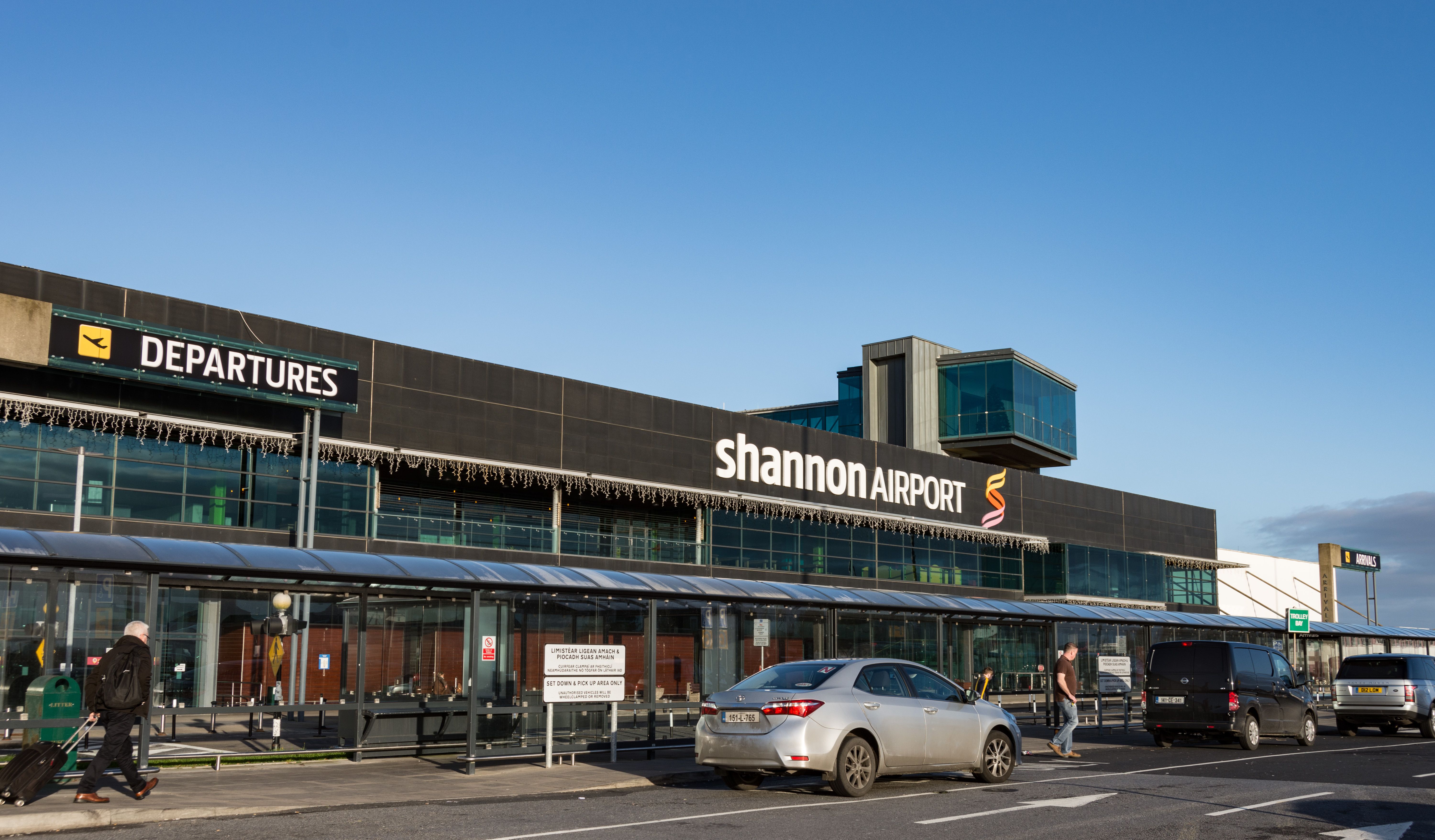 Several cars and travelers right outside the main entrance to Shannon Airport.