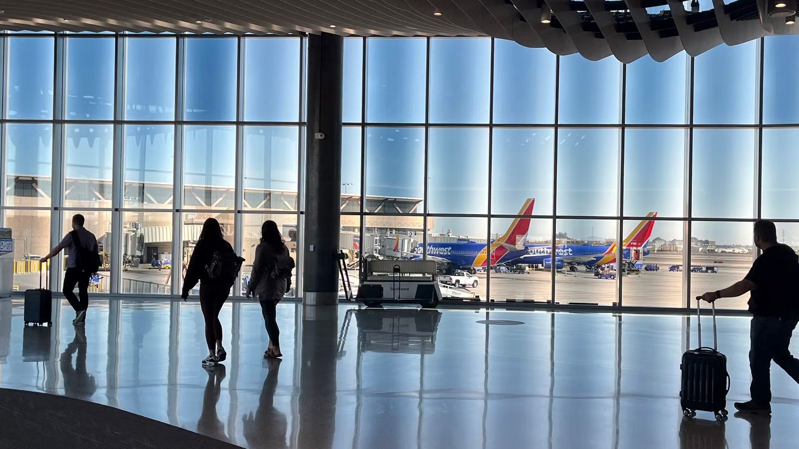 Passengers moving about an airport terminal near a window, where two Southwest Airlines aircraft can be seen on the apron.
