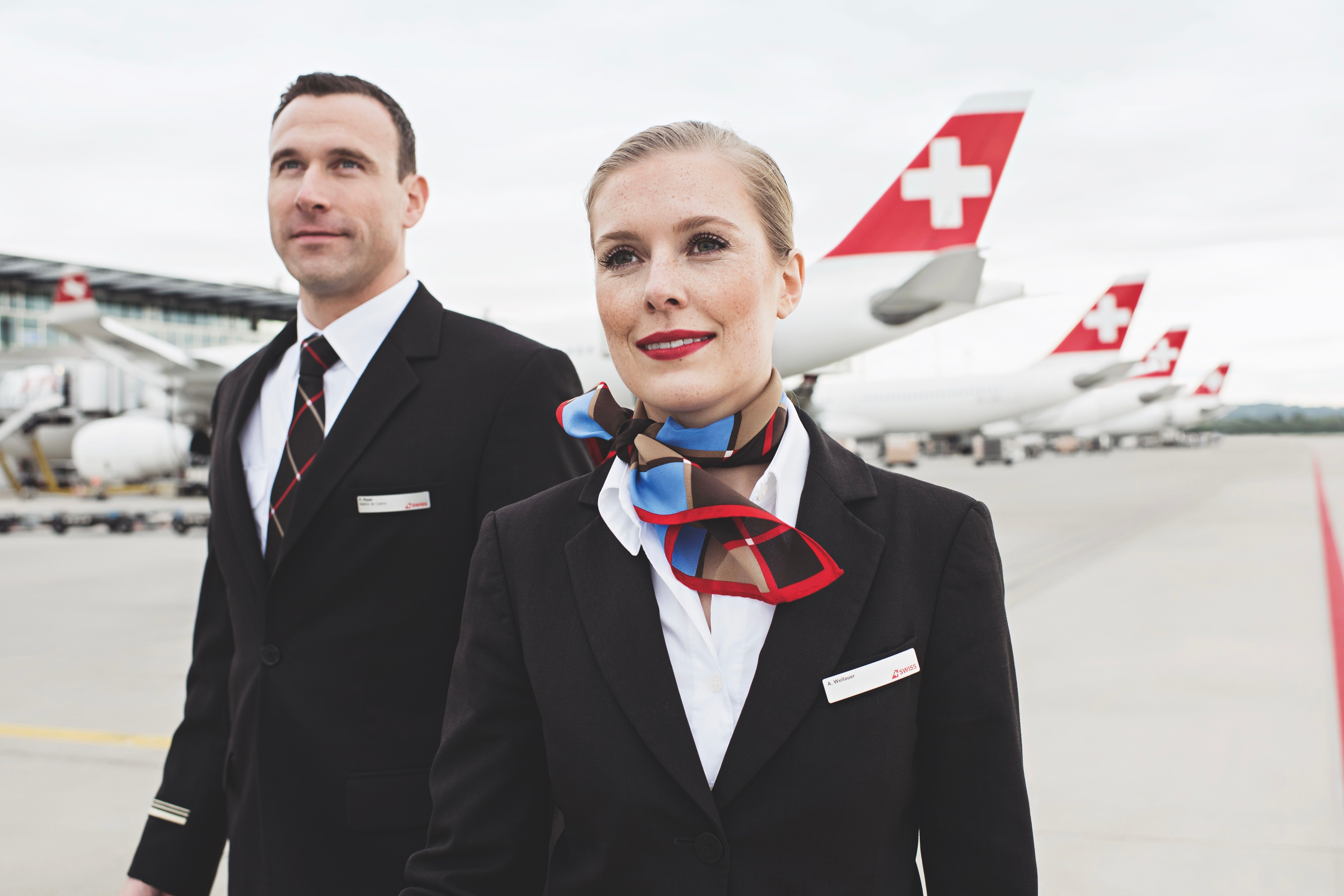 Two SWISS cabin crew members standing on the airport apron in front of several large aircraft.