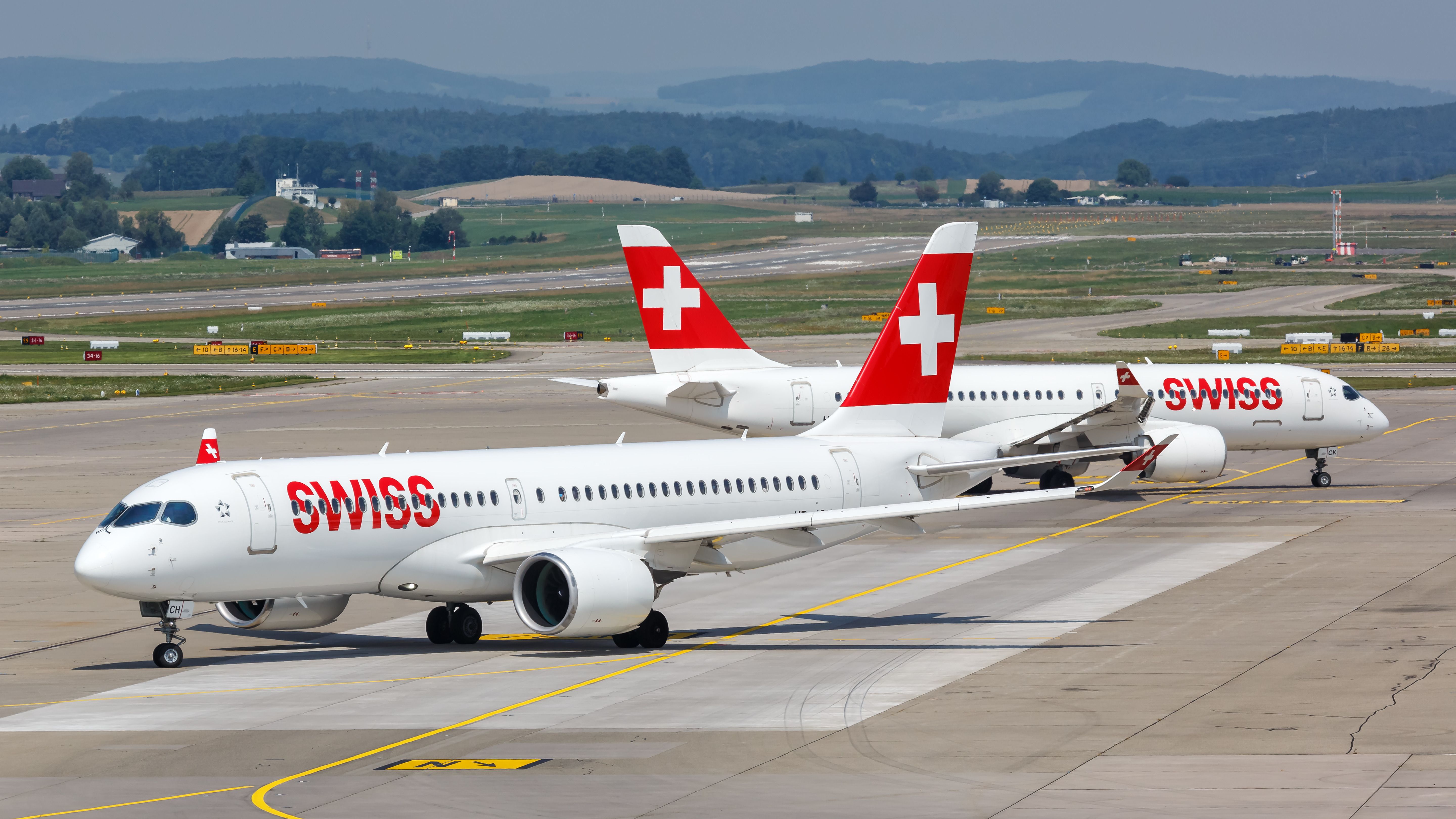 Two SWISS A220-300s taxiing on an airport apron.