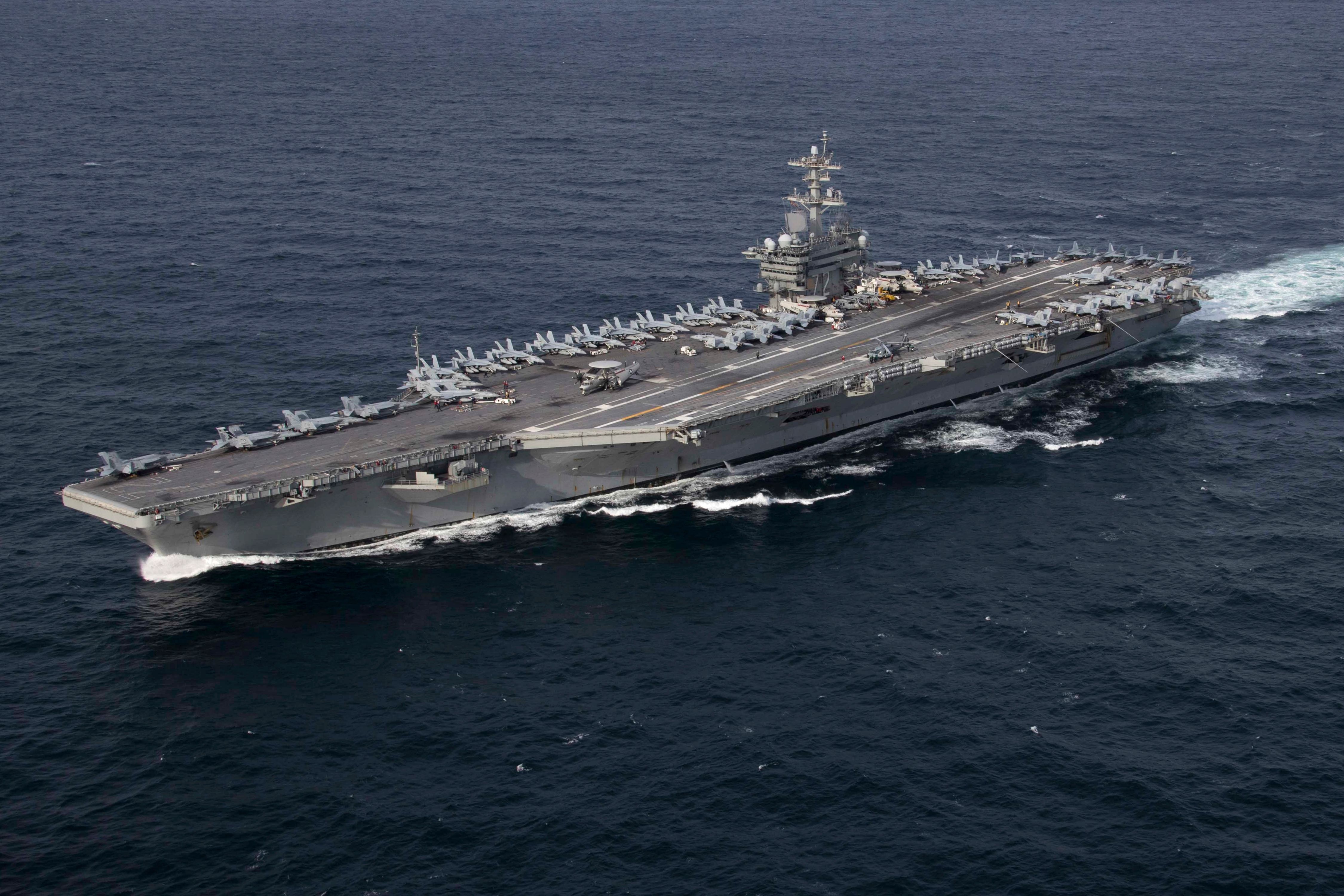 The USS Abraham Lincoln floating in water with many fighter jets on the deck.