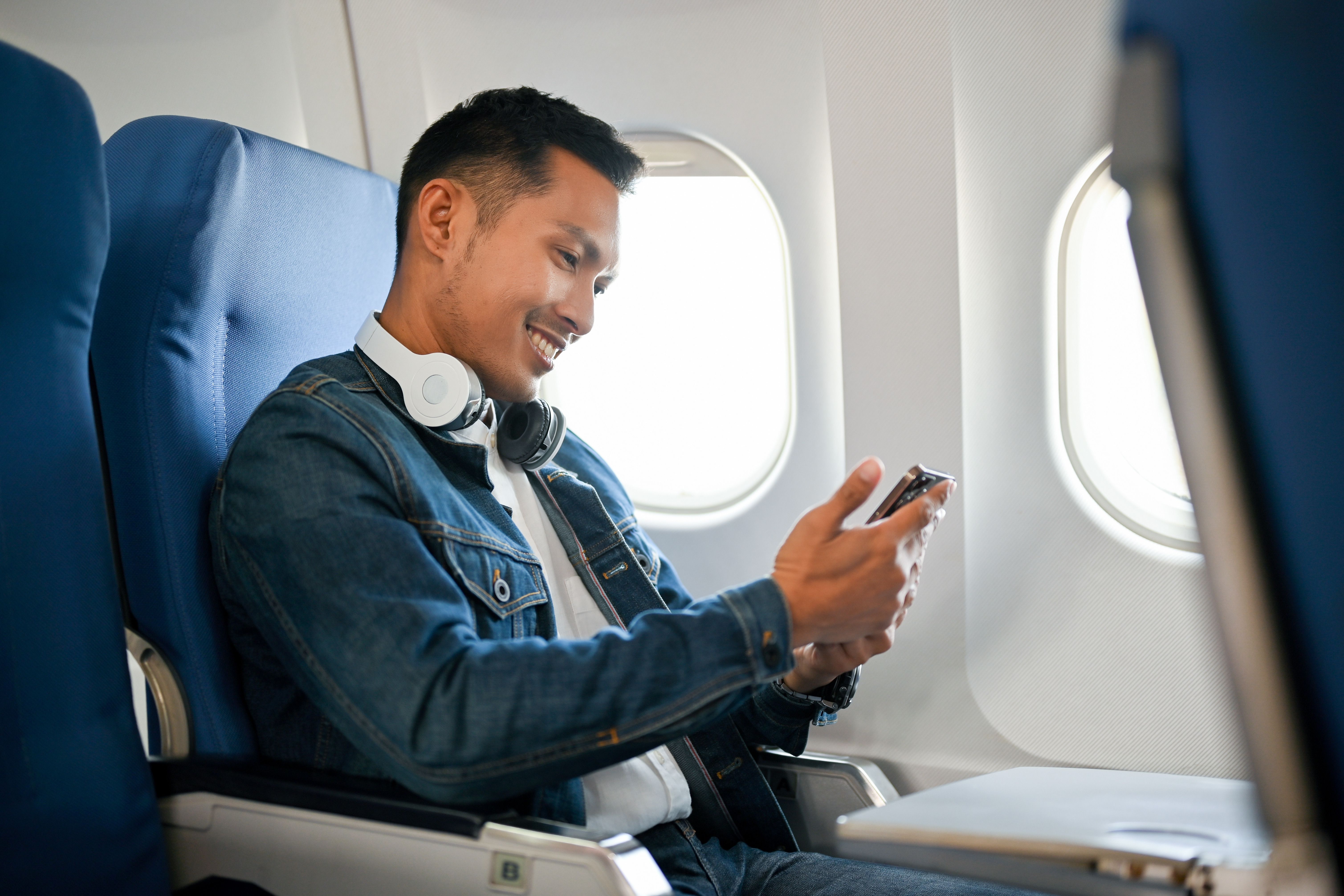 A man sitting in a window seat on an aircraft using his phone.
