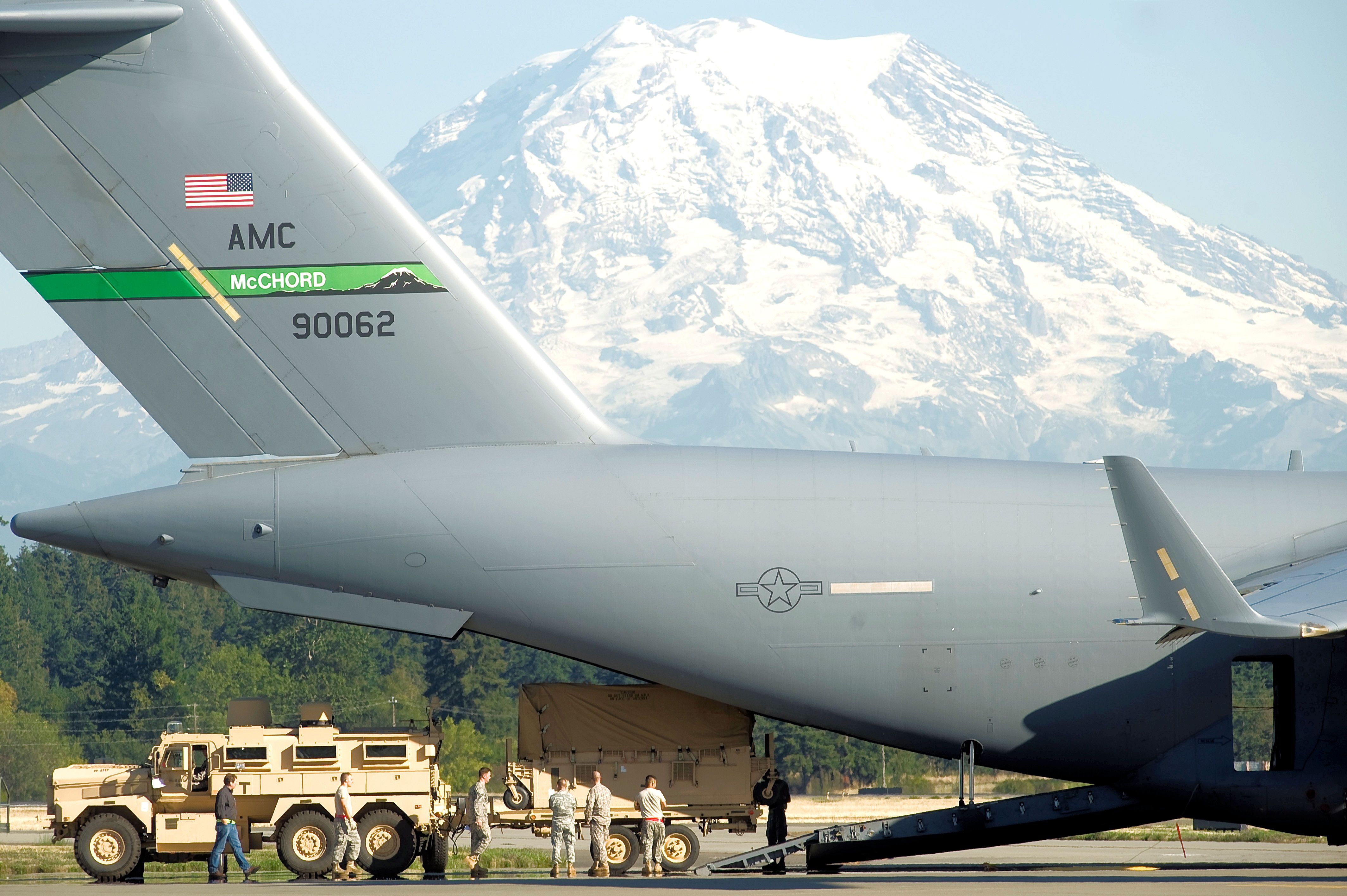 Army personnel loading a C-17 on an airfield apron.