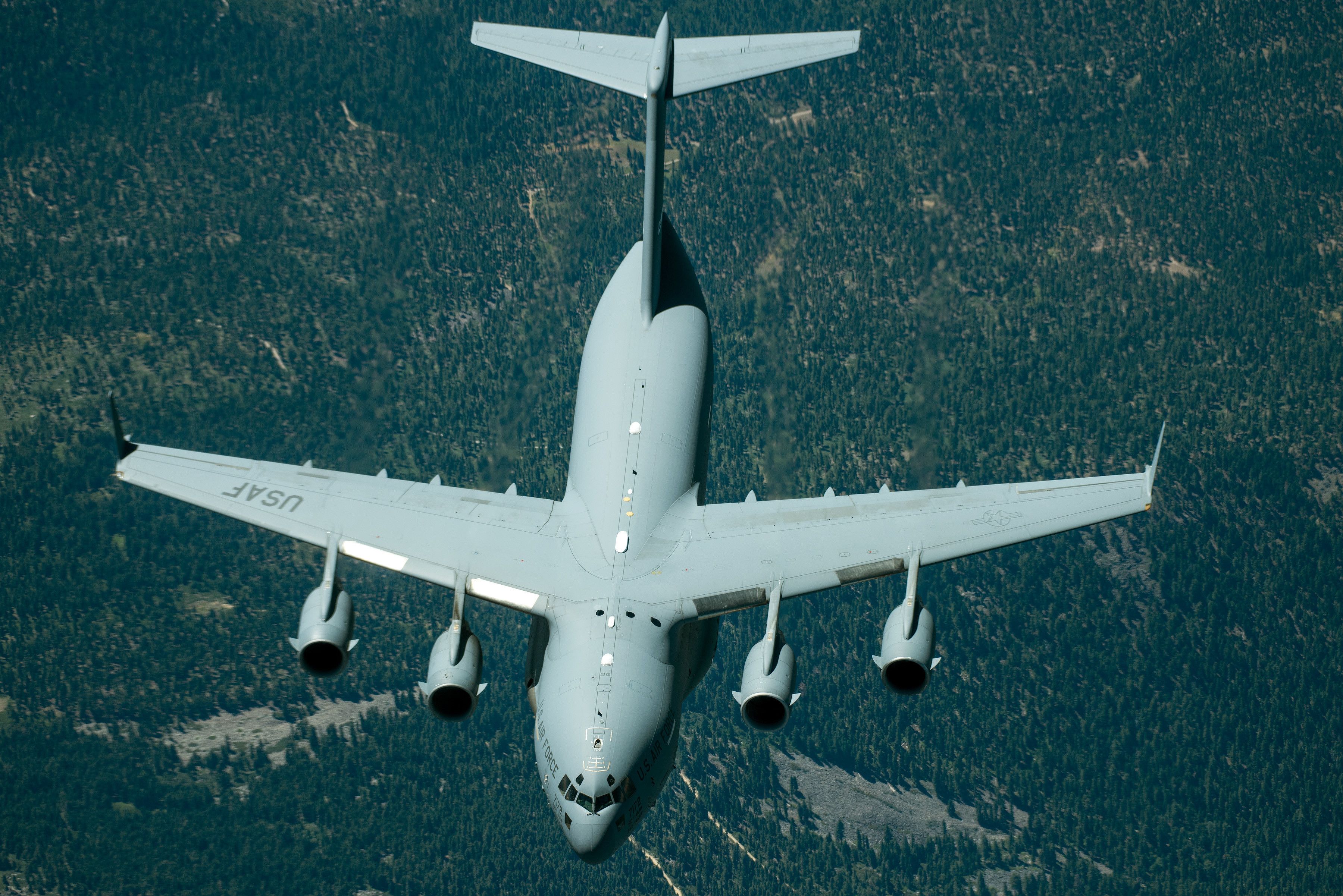 A C-17 Globemaster III flying over land, seen from above.