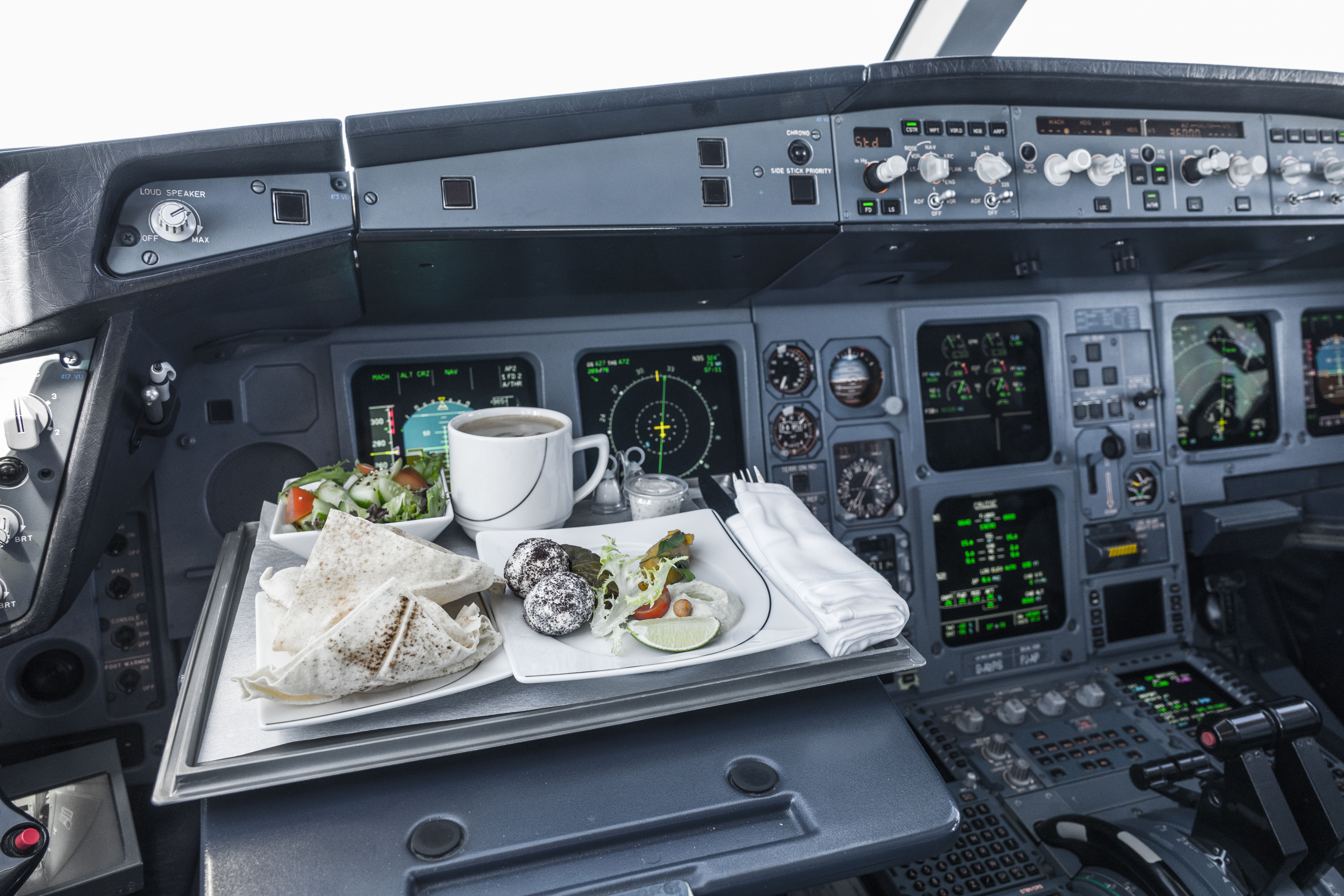 A meal on the tray table of the Captain's seat in a cockpit.