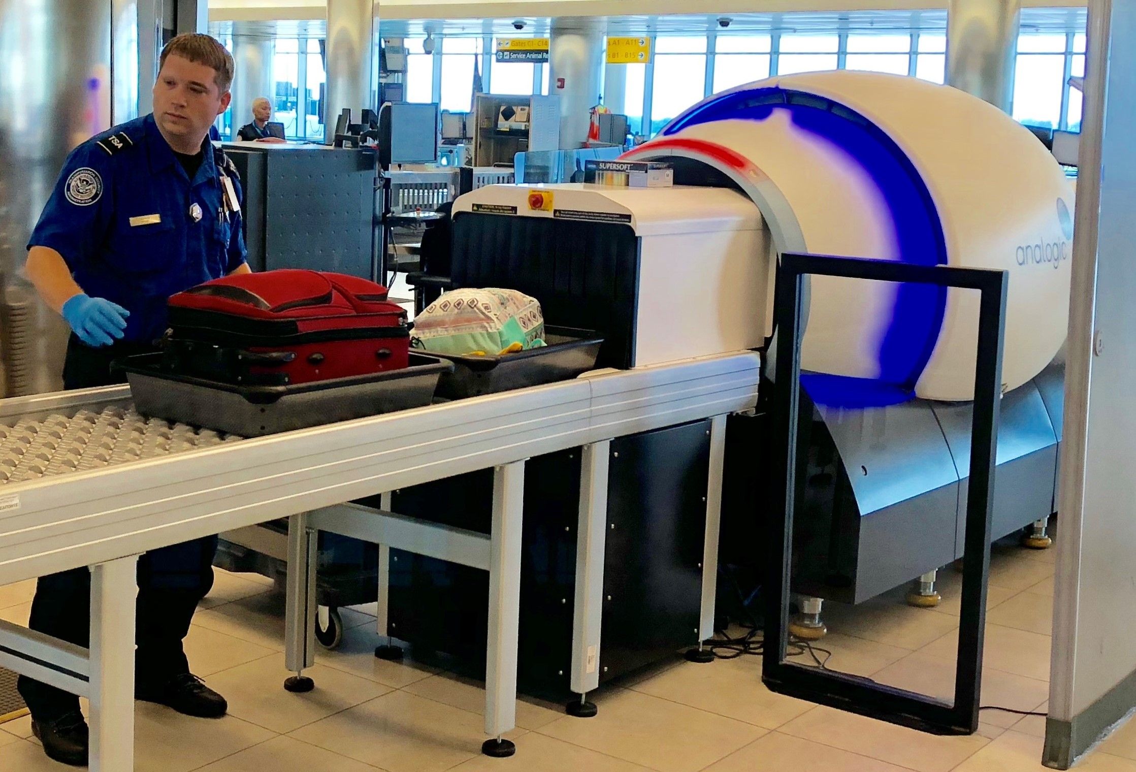 A TSA employee checking a screen as items go through an airport security CT scanner.