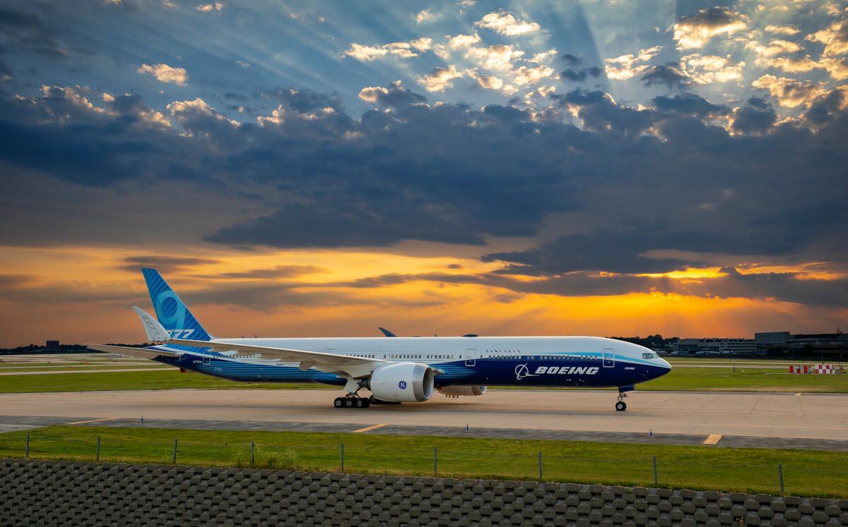Boeing 777-9 on tarmac with sunset in the background.