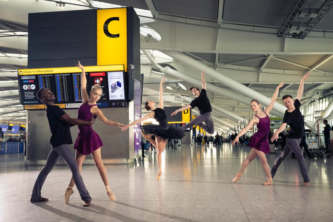 Several balet dancers in the check in area of Heathrow Airport.