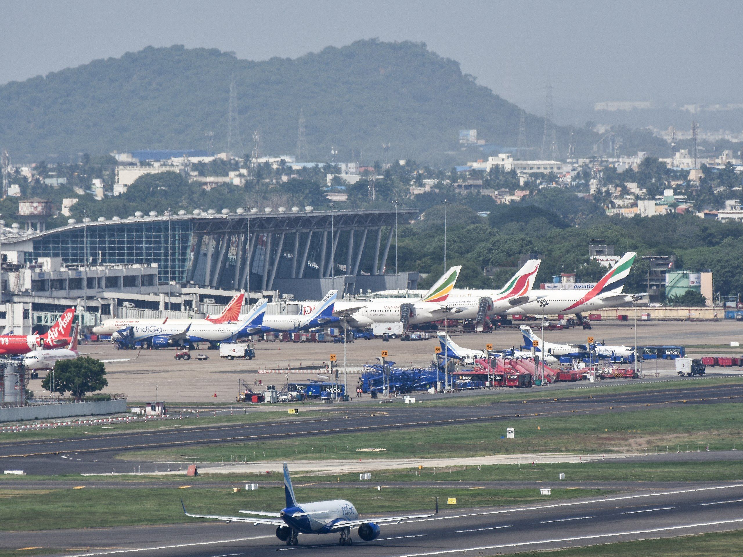 Several aircraft parked on the taxiway outside a terminal building with a mountain in the background
