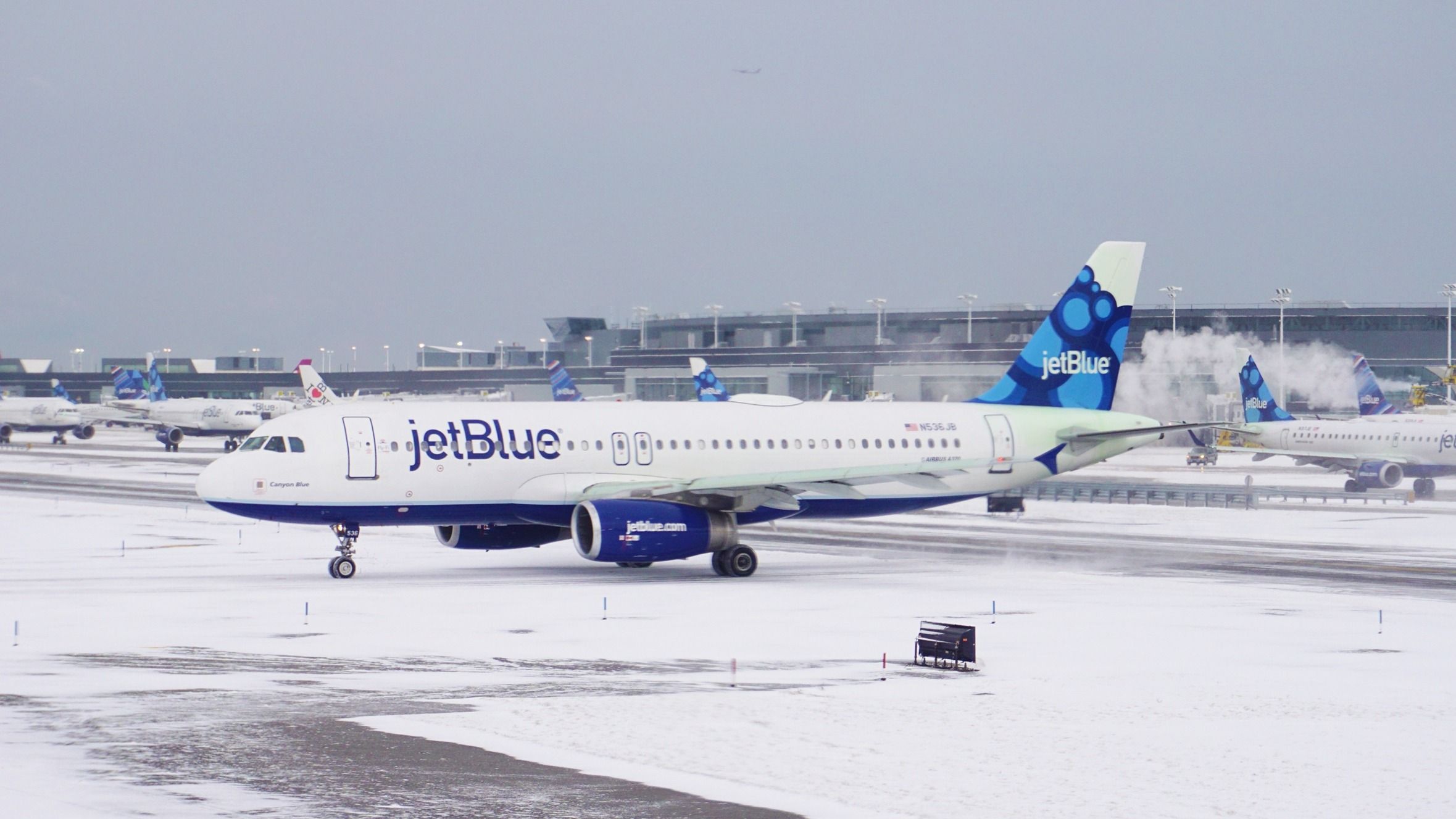 A JetBlue Airbus A320 on a wintery snowy airport apron.