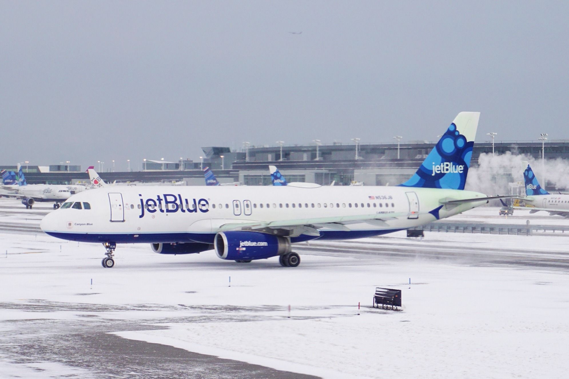 A JetBlue Airbus A320 on a wintery snowy airport apron.