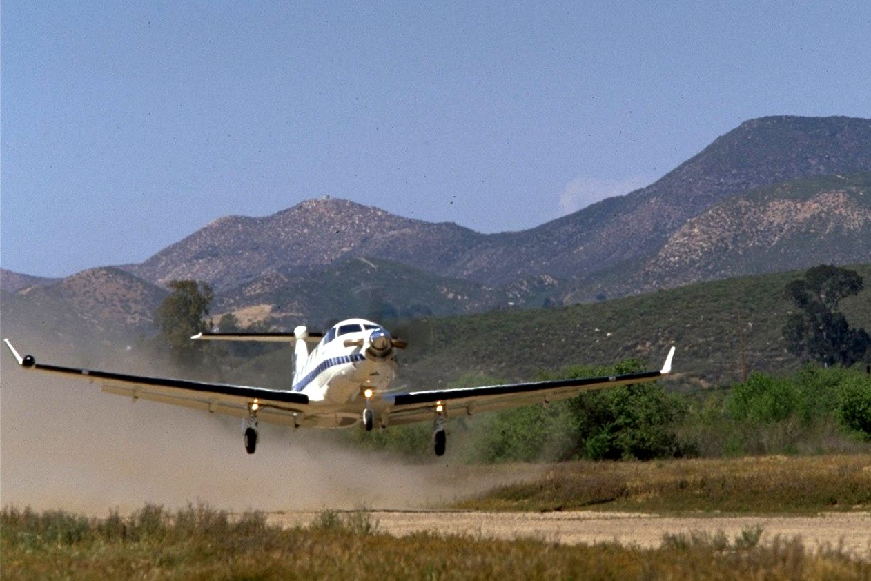 A PC-12 taking off from a dirt runway.