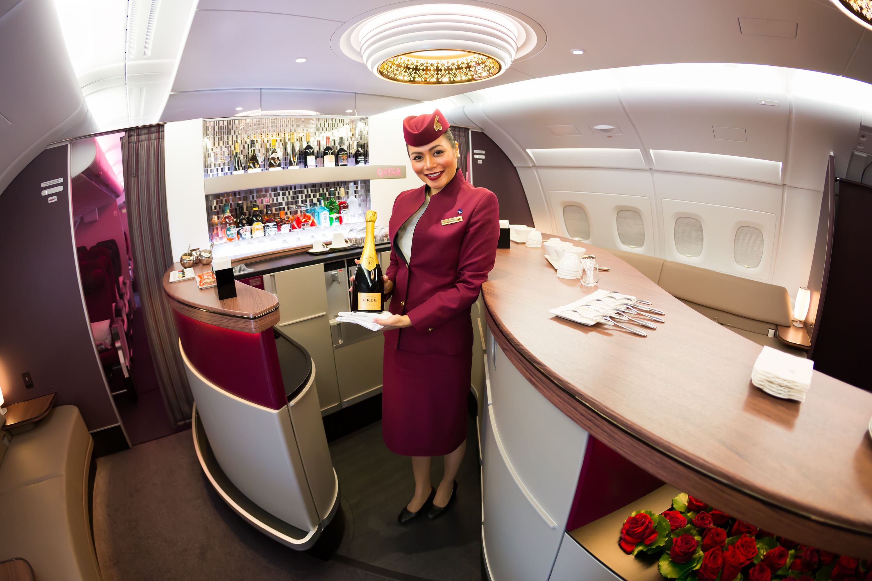 A Qatar Airways flight attendant preparing champagne in the bar area.