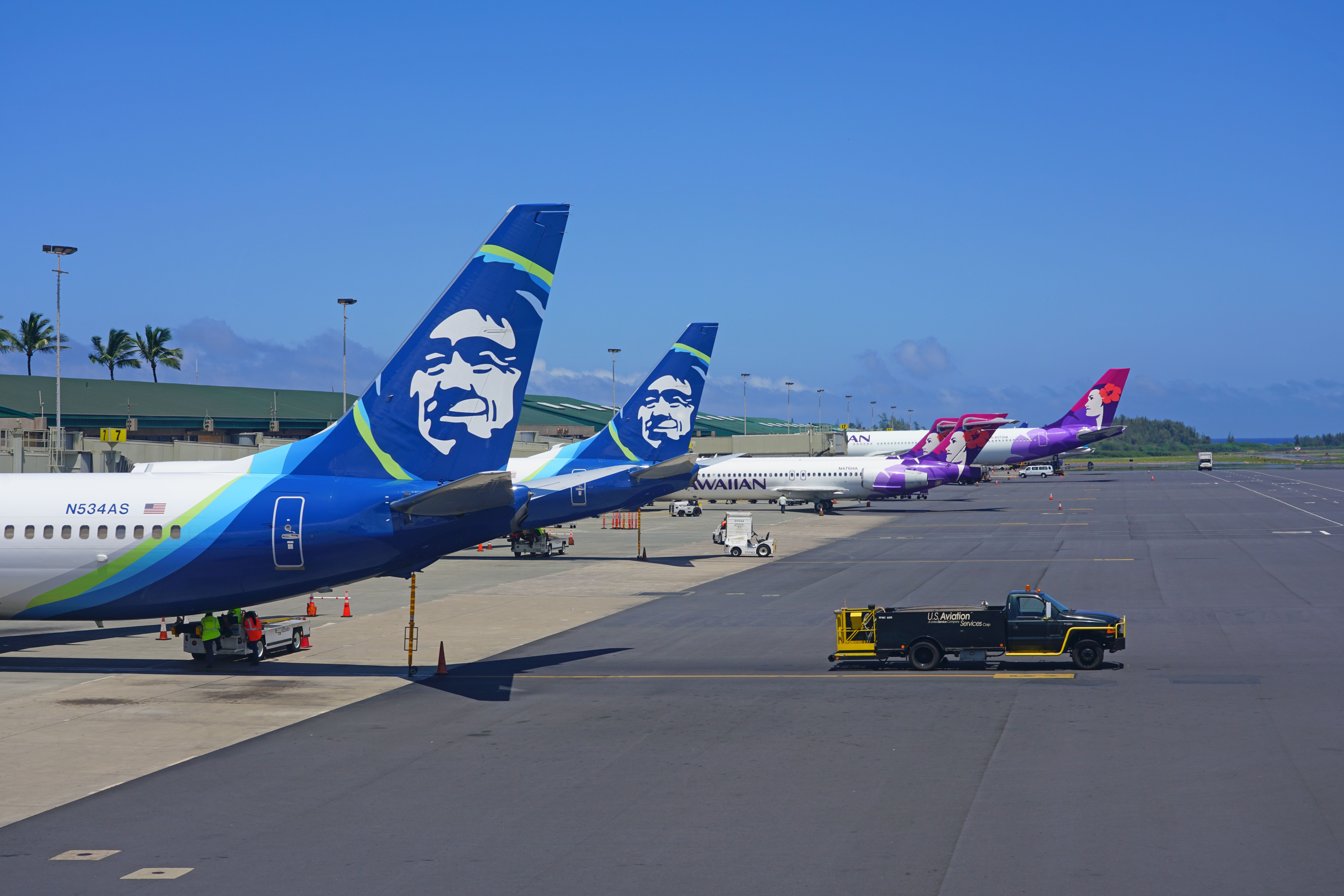 Two Alaska Airlines and two Hawaiian Airlines aircraft parked on an airport apron.
