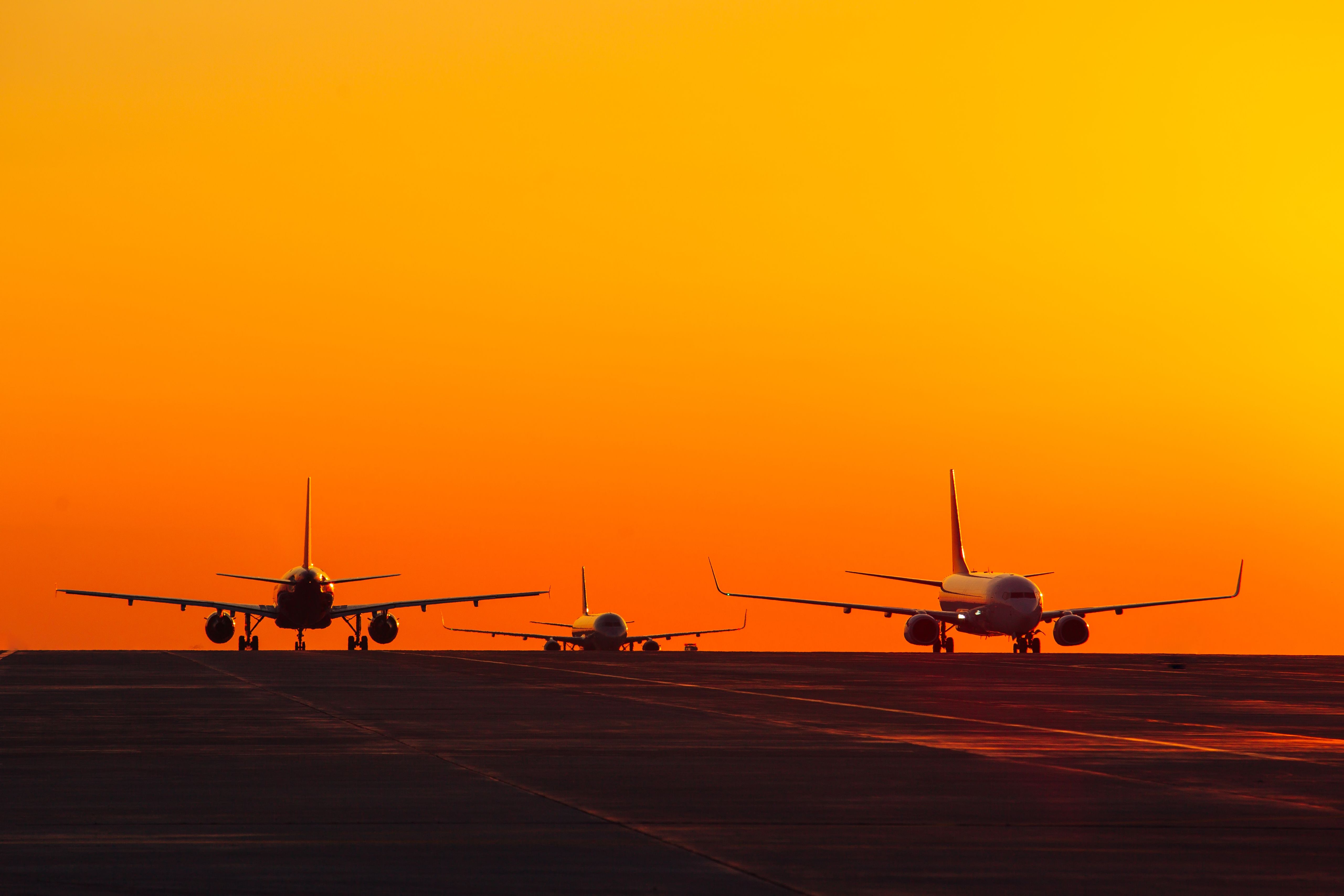 Three aircraft on an airport apron against a colorful sunset.