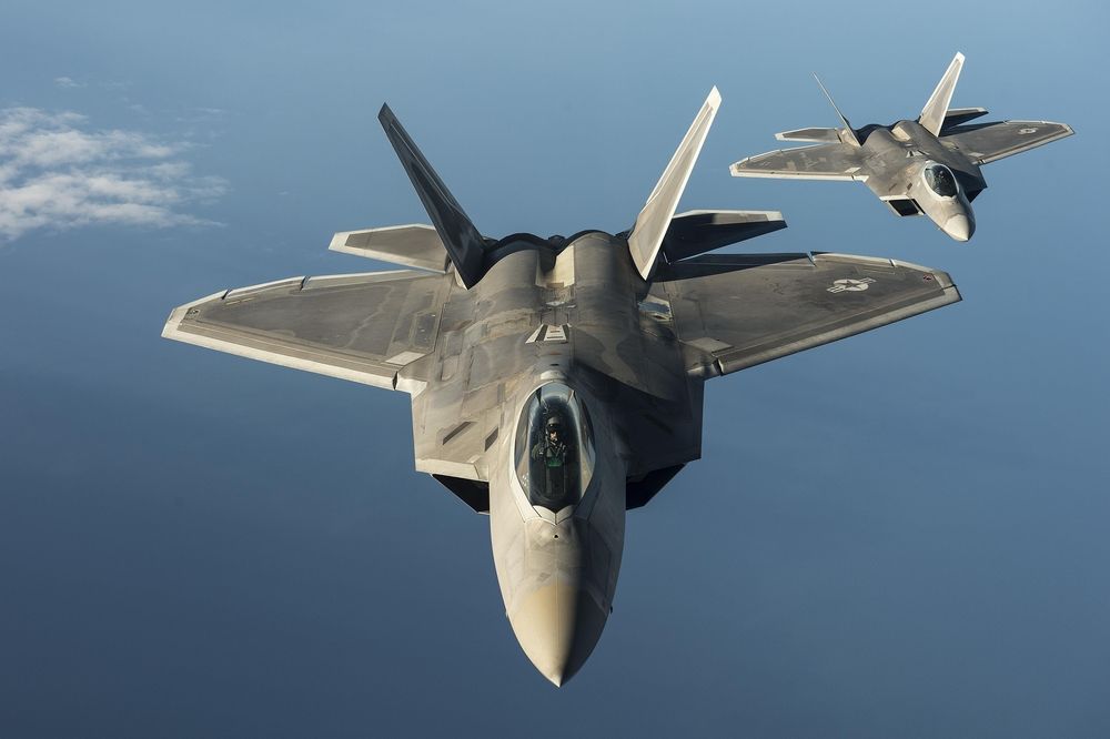 Two USAF F-22s flying over water.