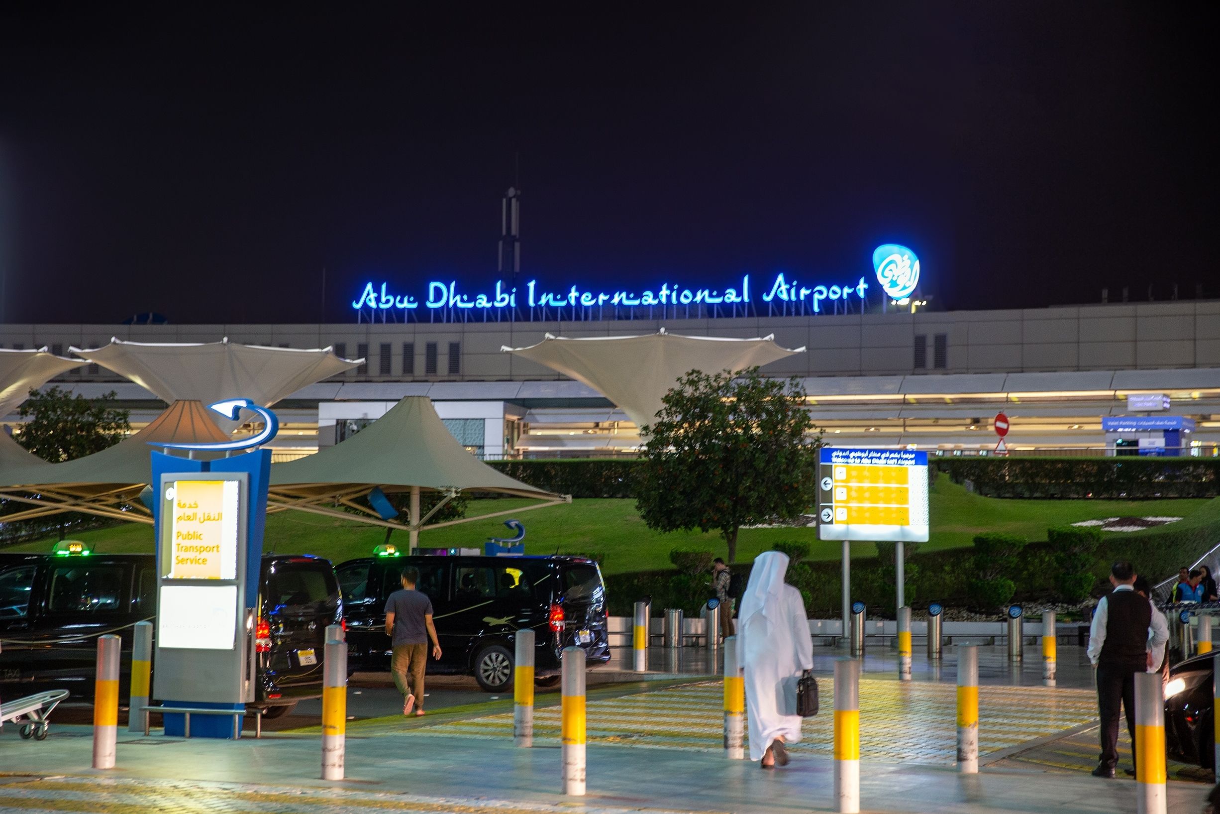 Passengers walking towards the main entrance to Abu Dhabi International Airport at night.