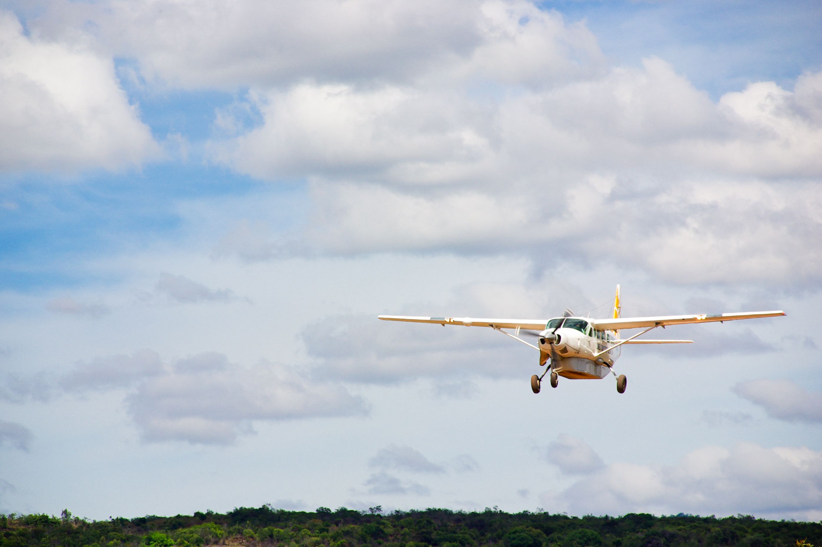 Small white plane with propeller in cloudy sky over jungle.