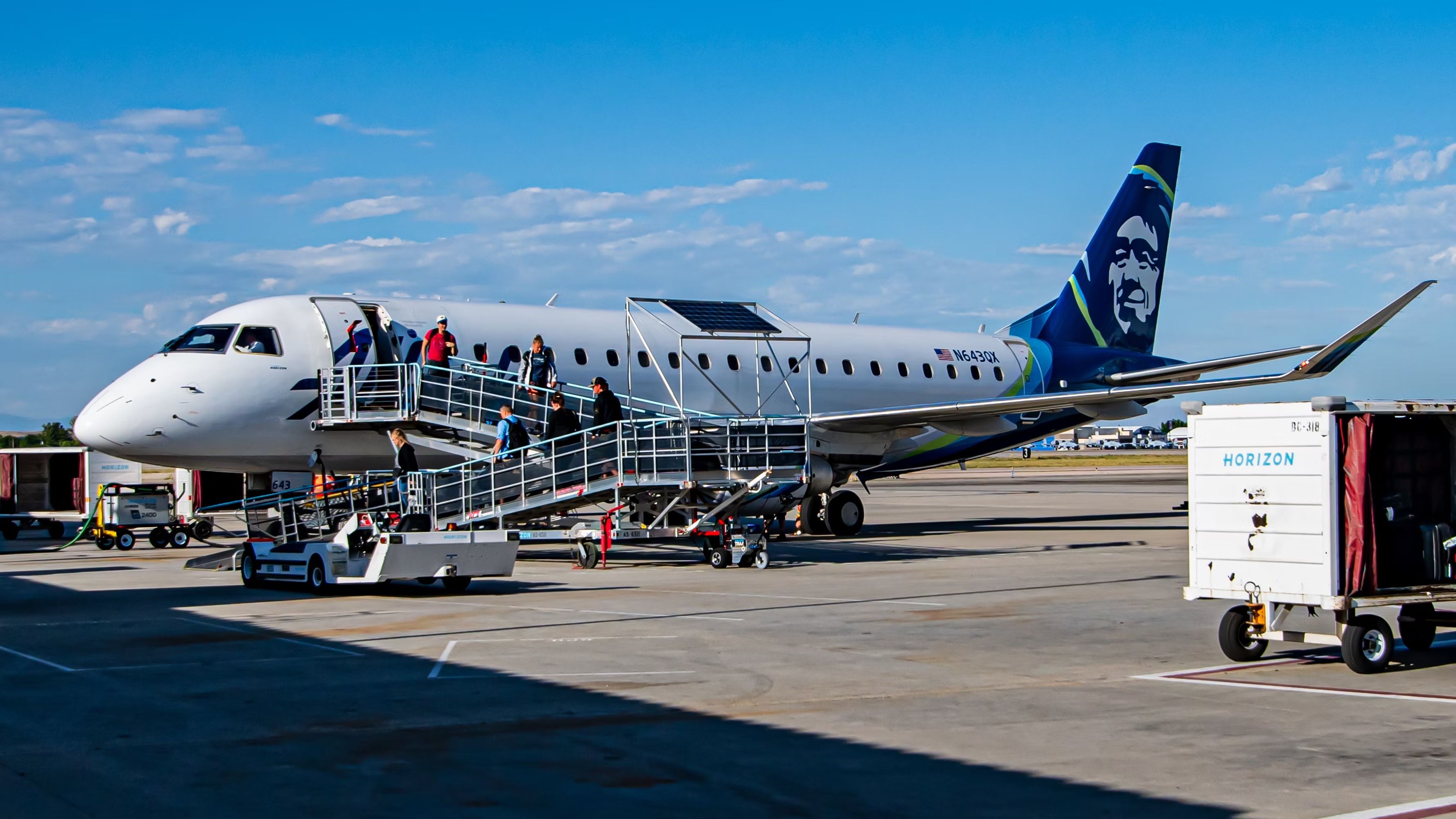 Passengers exiting a Horizon Air E175 parked on an airport apron.